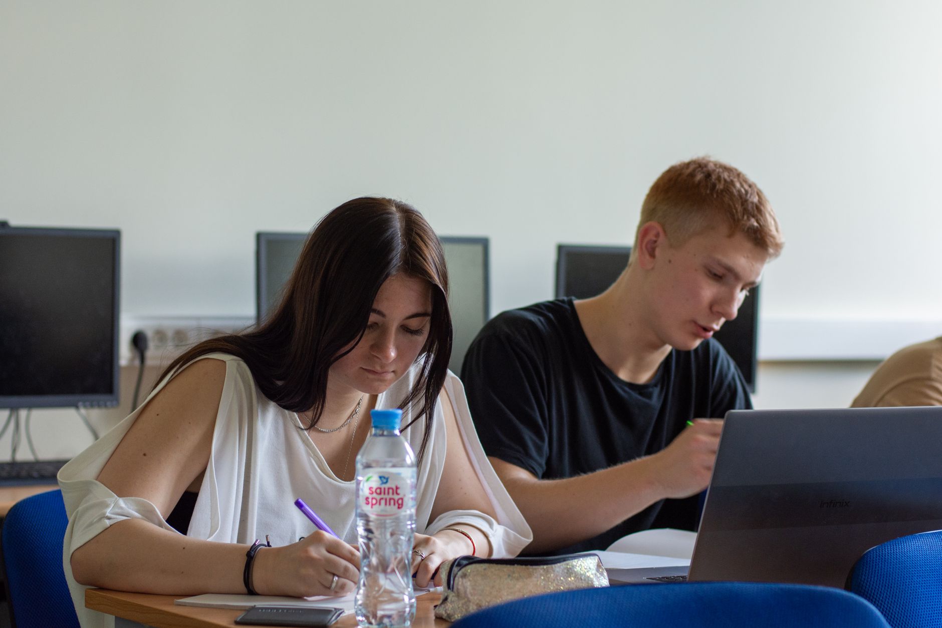 Qualifi Level 3 Extended Diploma in Business, Management and Study Skills — Two students focused on studying in a computer lab, using a laptop and taking notes.
