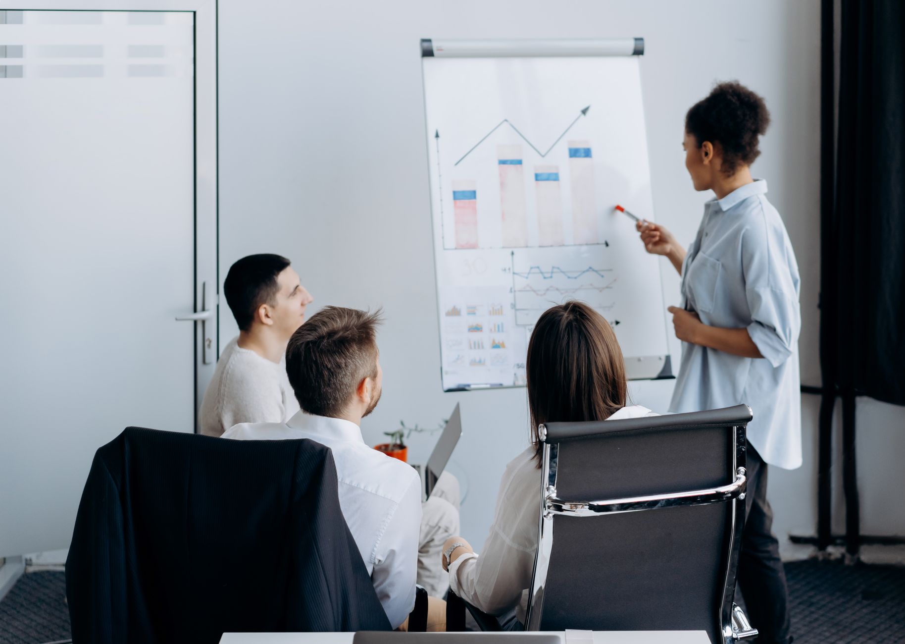 Qualifi Level 3 Extended Diploma in Business Management — Business team in meeting with presenter discussing charts on a flip board.