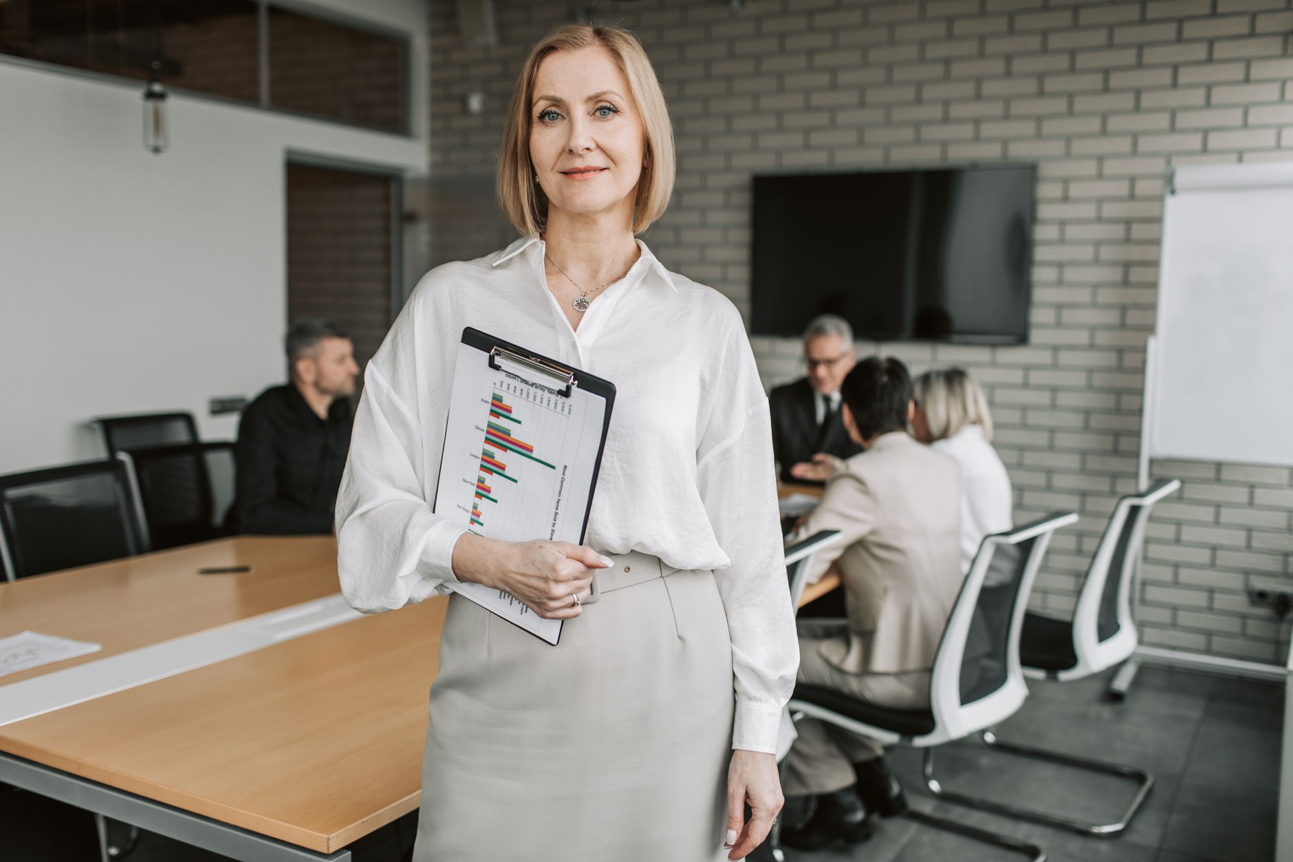 Qualifi Level 7 Diploma in Strategic Management and Leadership — Professional businesswoman holding a clipboard during an office meeting, showcasing leadership in a corporate environment.
