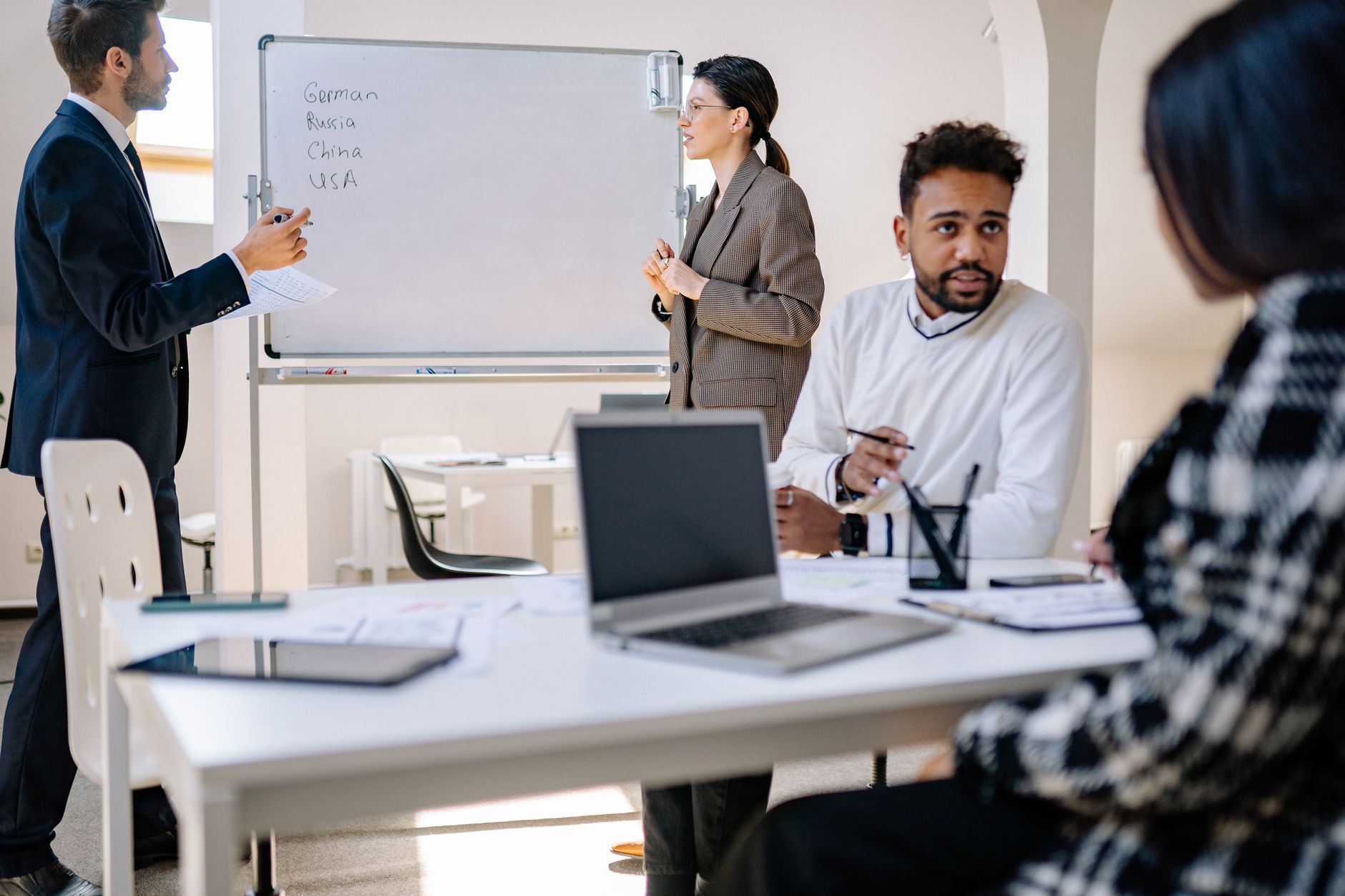 Qualifi Level 7 Certificate in International Business Strategy — A diverse group of professionals engaged in a collaborative office meeting with laptops and a whiteboard.