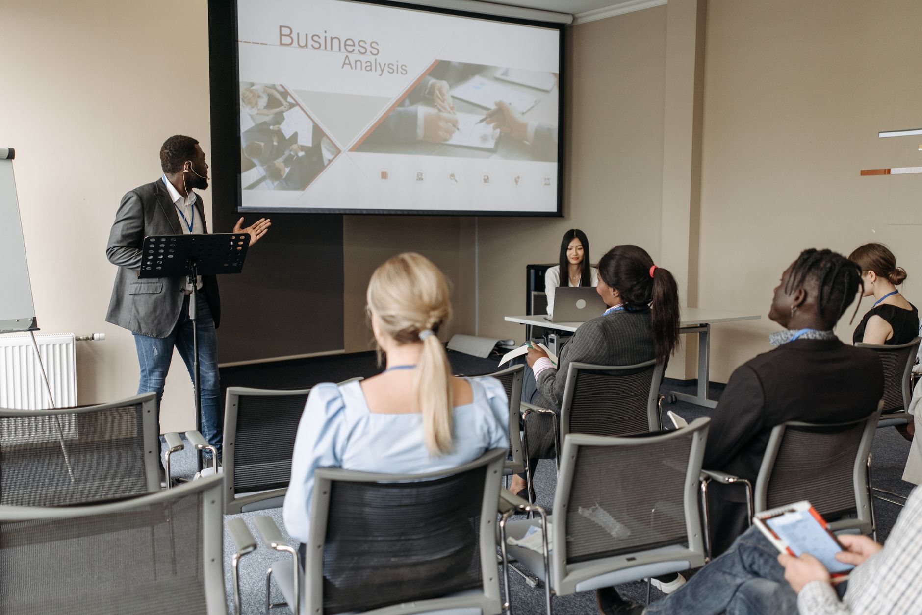 Qualifi Level 7 Diploma in Strategic Marketing — A diverse group attends a business analysis seminar with a presenter and projection screen in a modern conference room.