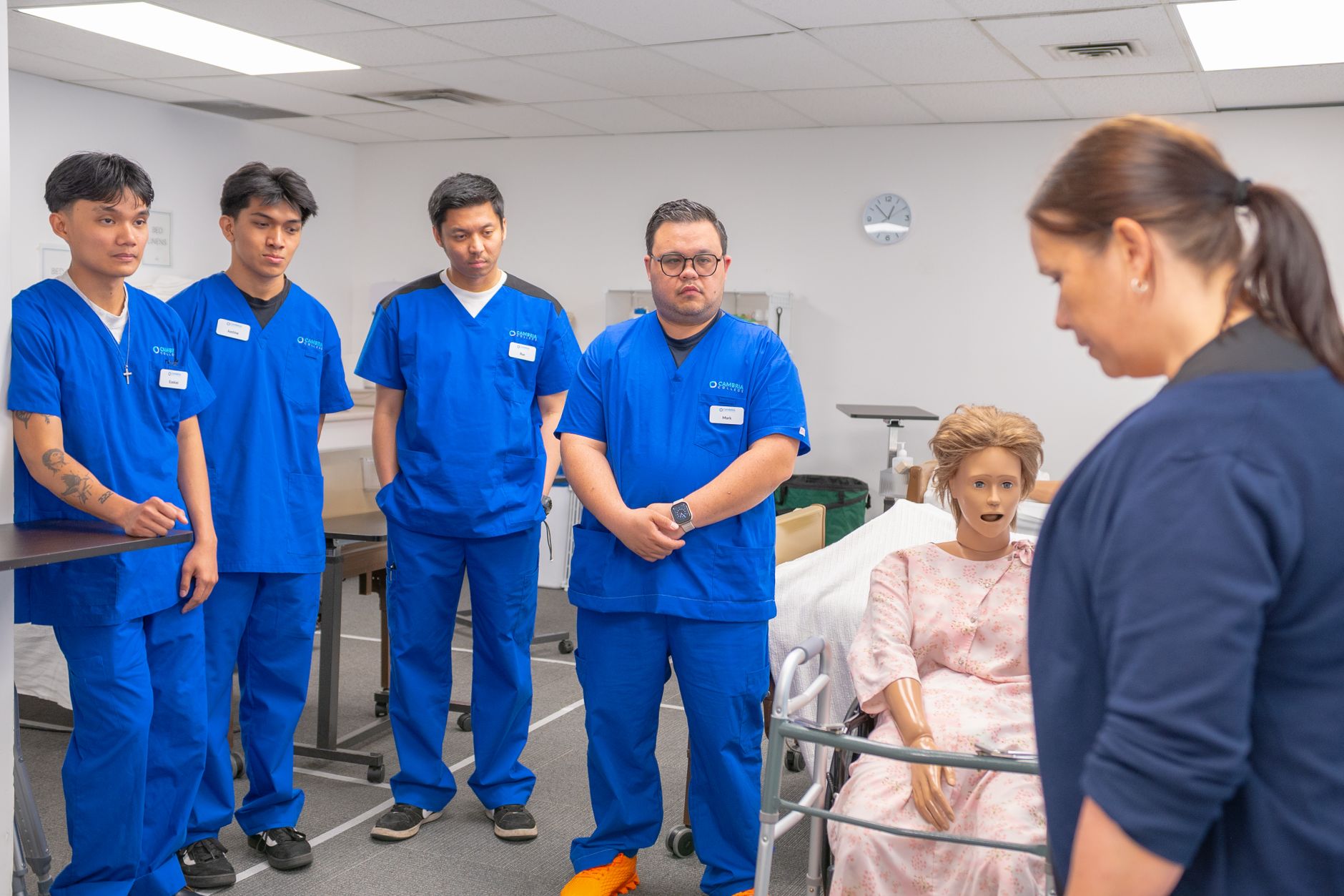 Qualifi Level 2 Adult Social Care Certificate — Nursing students in blue scrubs practicing patient care using a medical mannequin.