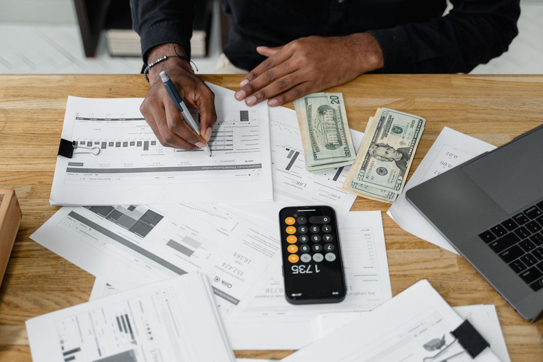 Qualifi Level 5 Extended Diploma in Accounting and Finance — Man working on financial reports with calculator, money, and laptop on a desk.