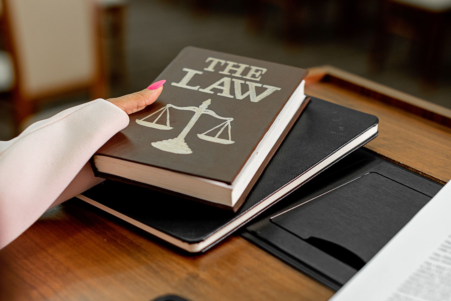 Qualifi Level 4 Diploma in Law — Closeup image of a law book titled 'The Law' on a wooden desk with scales of justice.