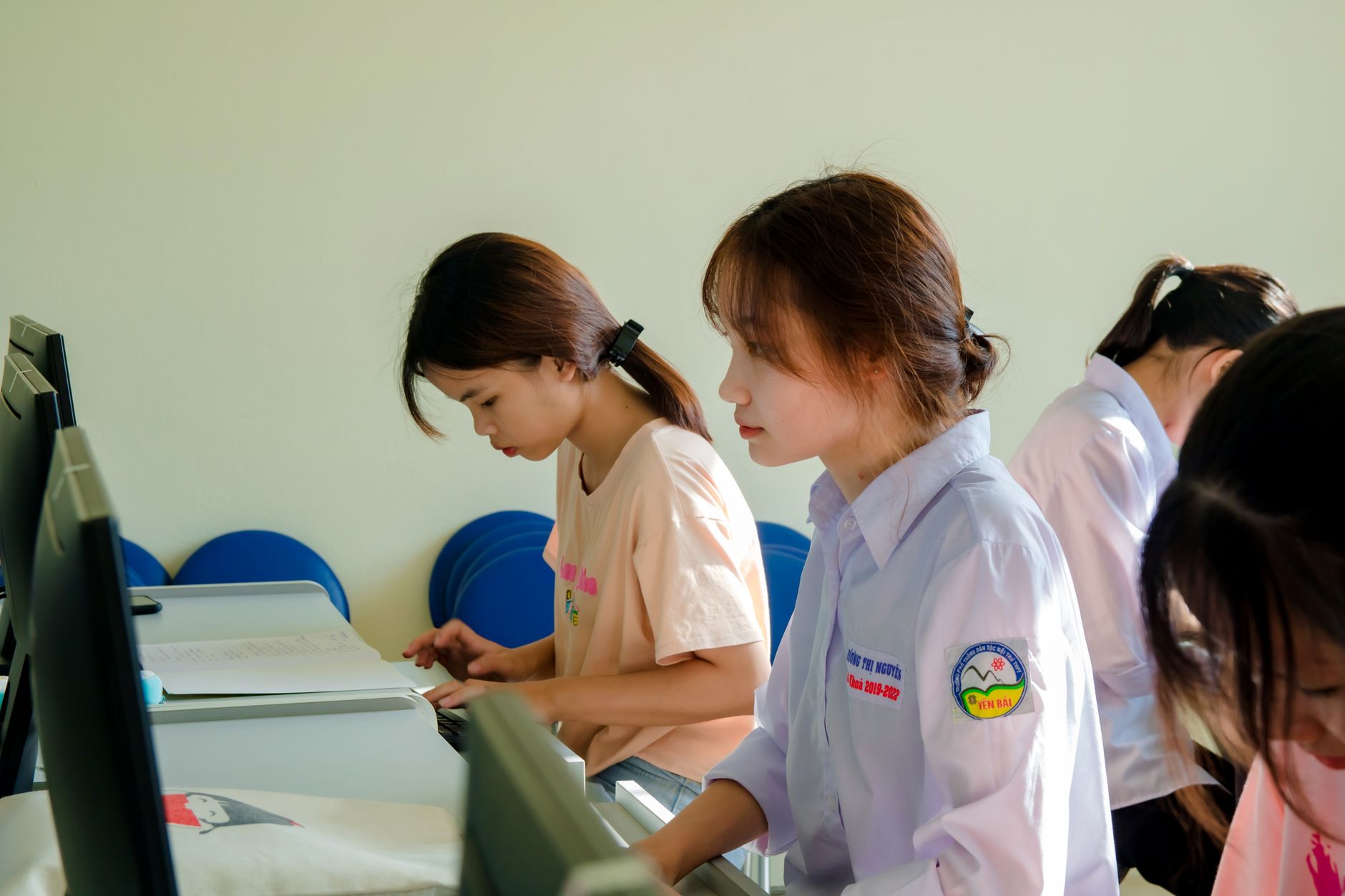 Qualifi Level 3 Extended Diploma in IT and Cyber Security — Three young women concentrating on a computer task in a classroom setting.