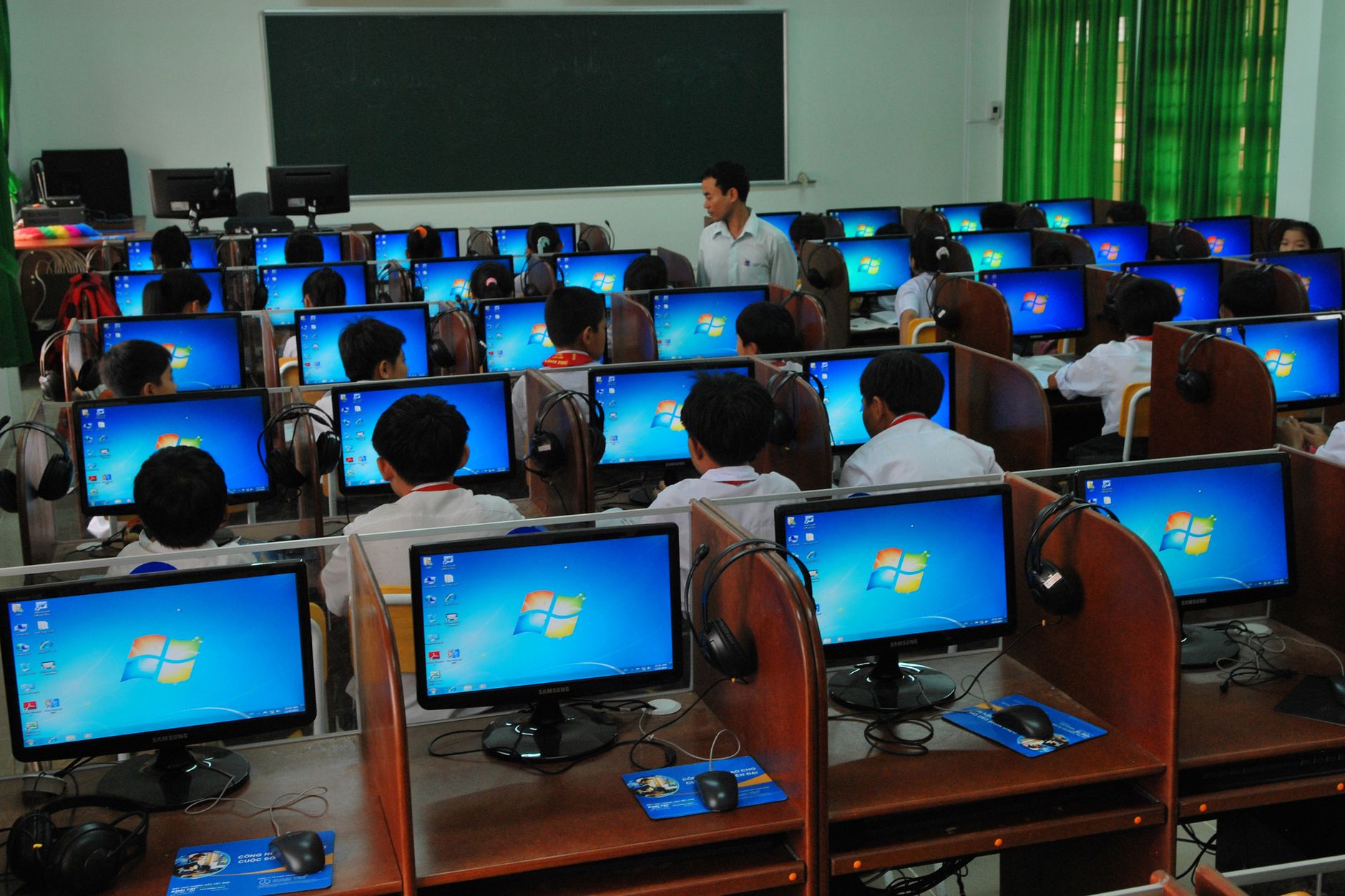 Qualifi Level 4 Diploma in IT – Networking — Students learning in a computer lab with multiple monitors and a teacher instructing.