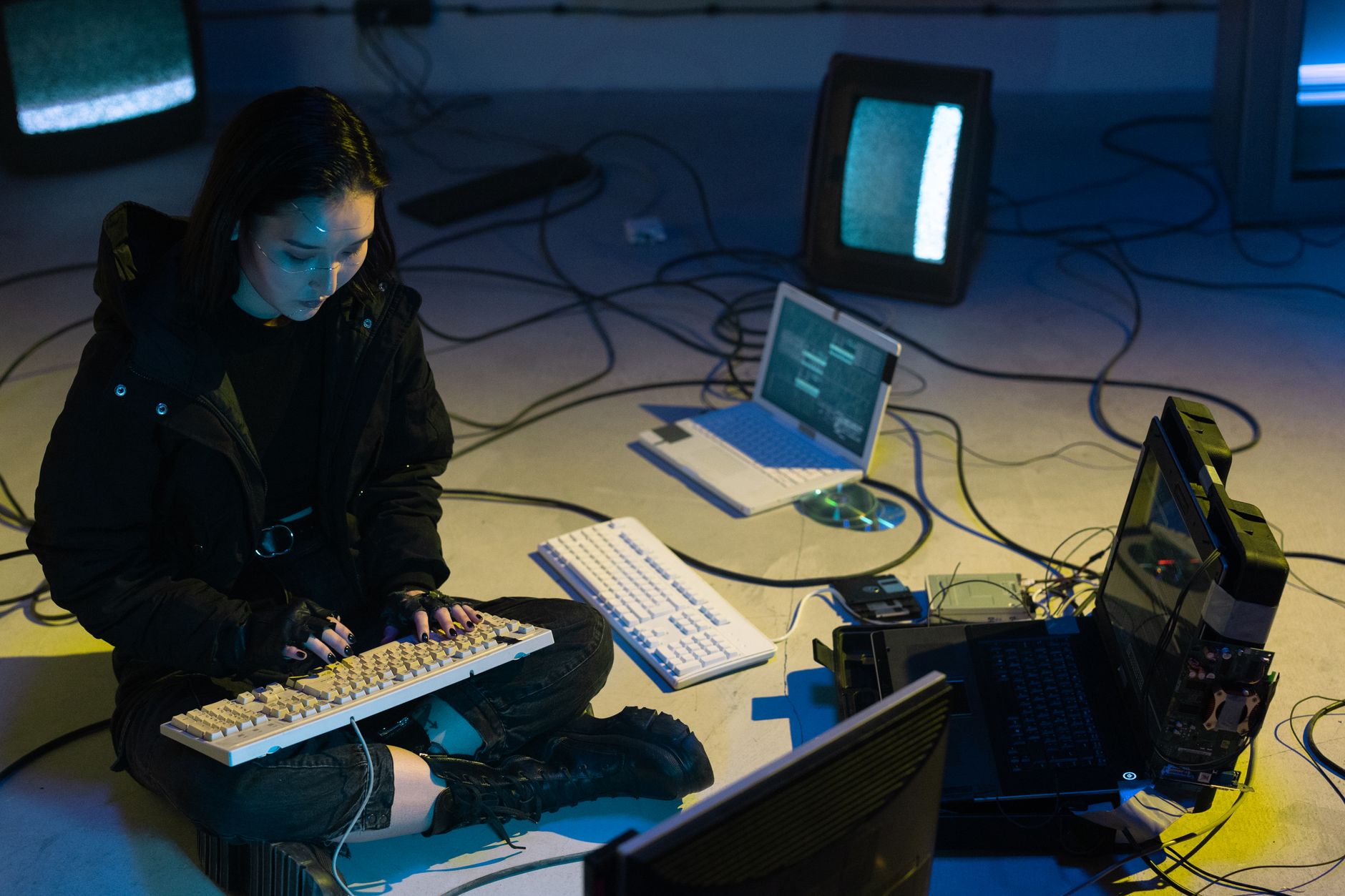 Qualifi Level 5 Extended Diploma in Networking and Cyber Security — Young Asian woman engaged in computer hacking in a dimly lit, technologically equipped room.