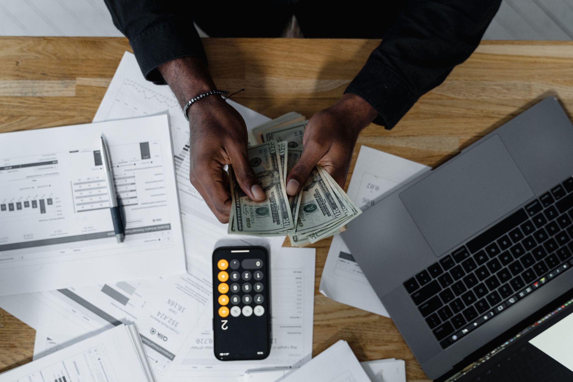 An Introduction to Finance — Person counting US dollars, using a calculator and laptop, with financial documents on a wooden desk.