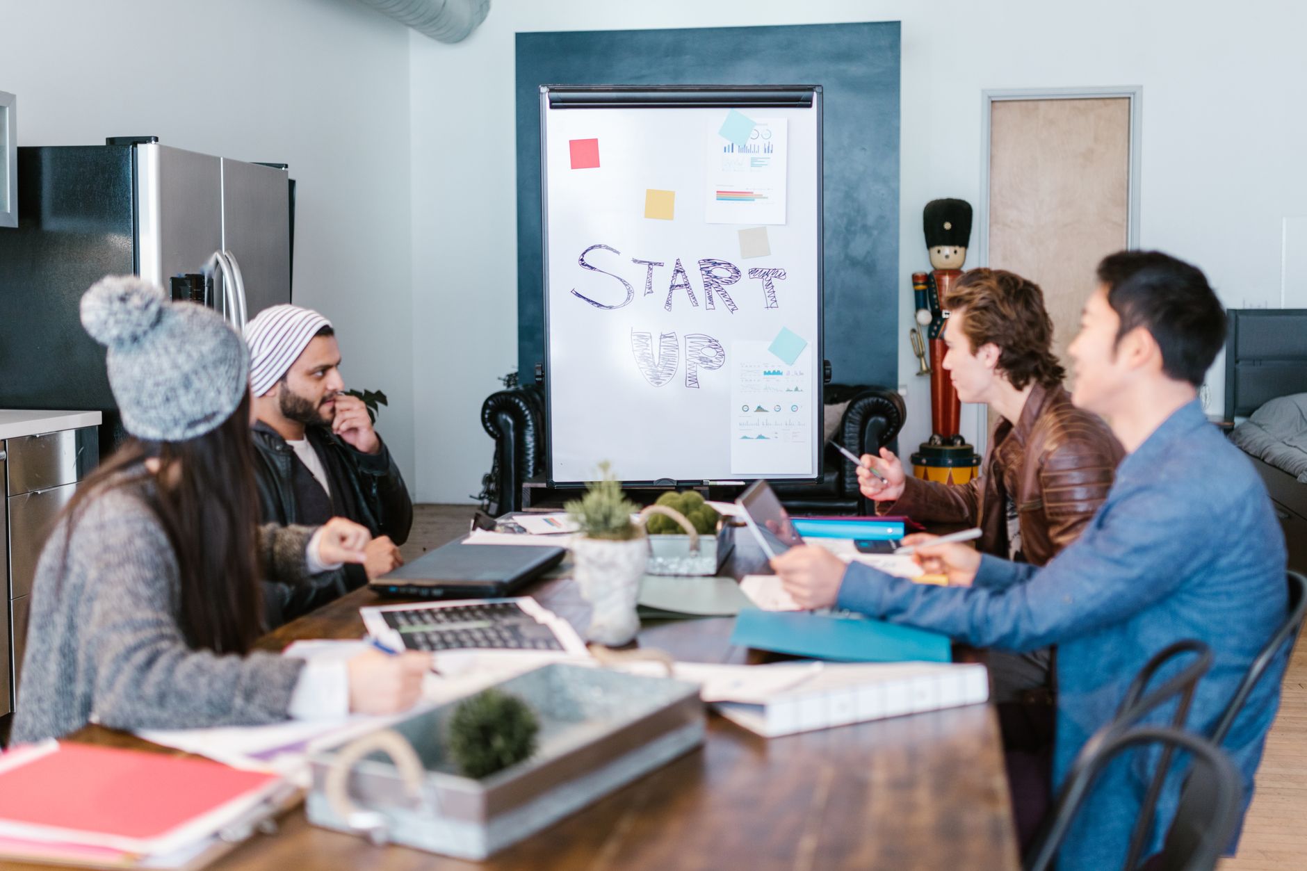 Entrepreneurship and Entrepreneurial Business Planning — A diverse group of adults working around a table in a startup office, planning and discussing ideas.