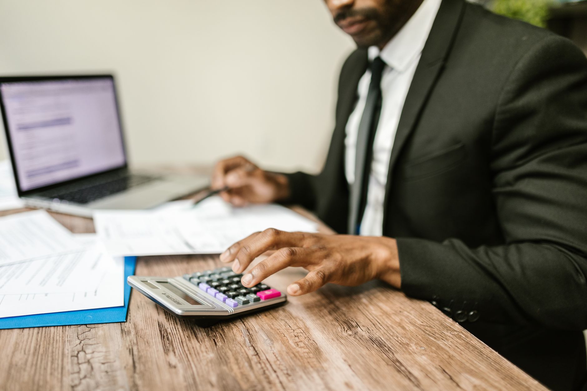 Financial Awareness — A businessman in a black suit using a calculator at a desk with financial documents and a laptop.