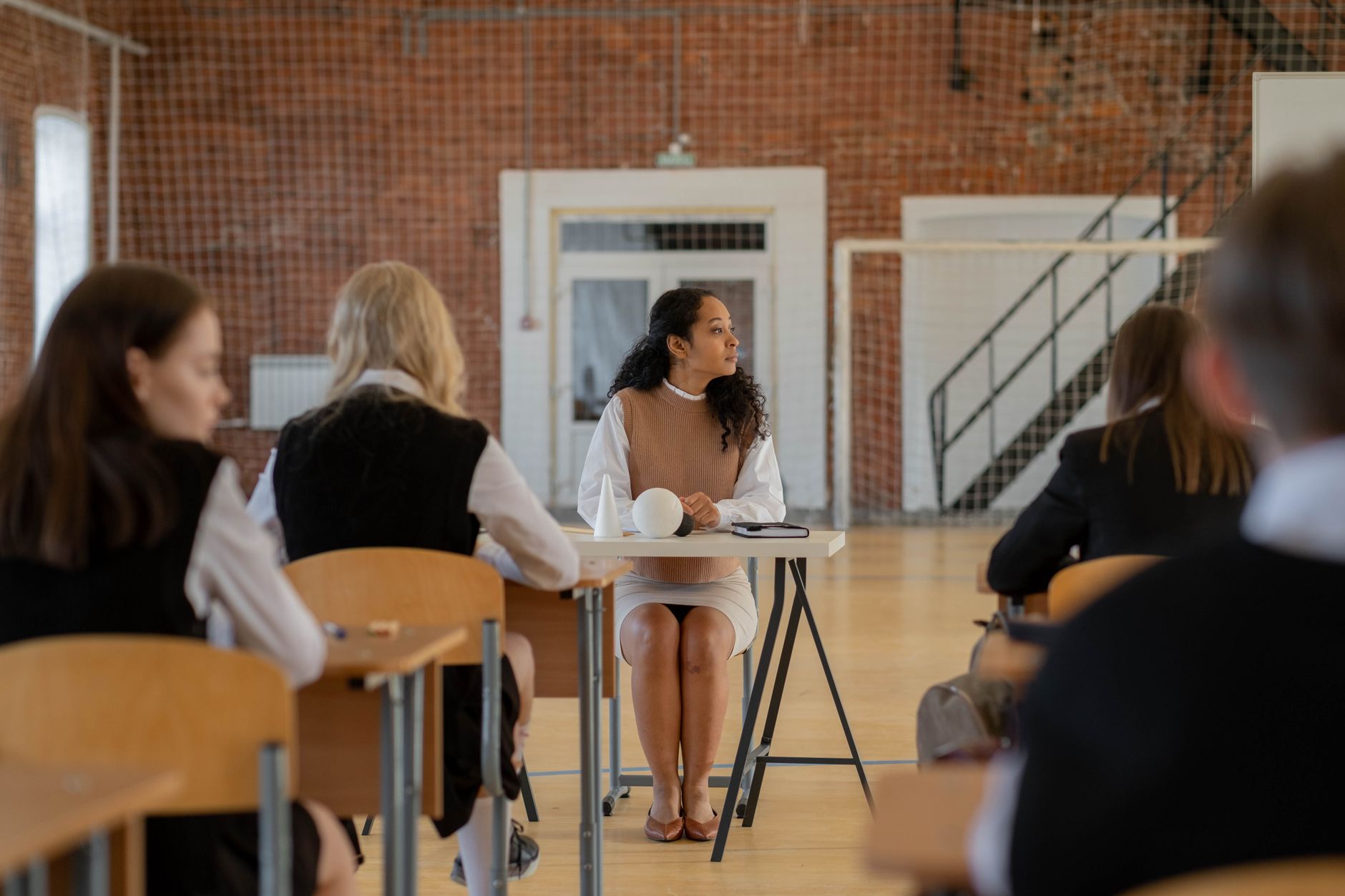 Managing Change — Teacher sitting at desk during class in a school gymnasium.