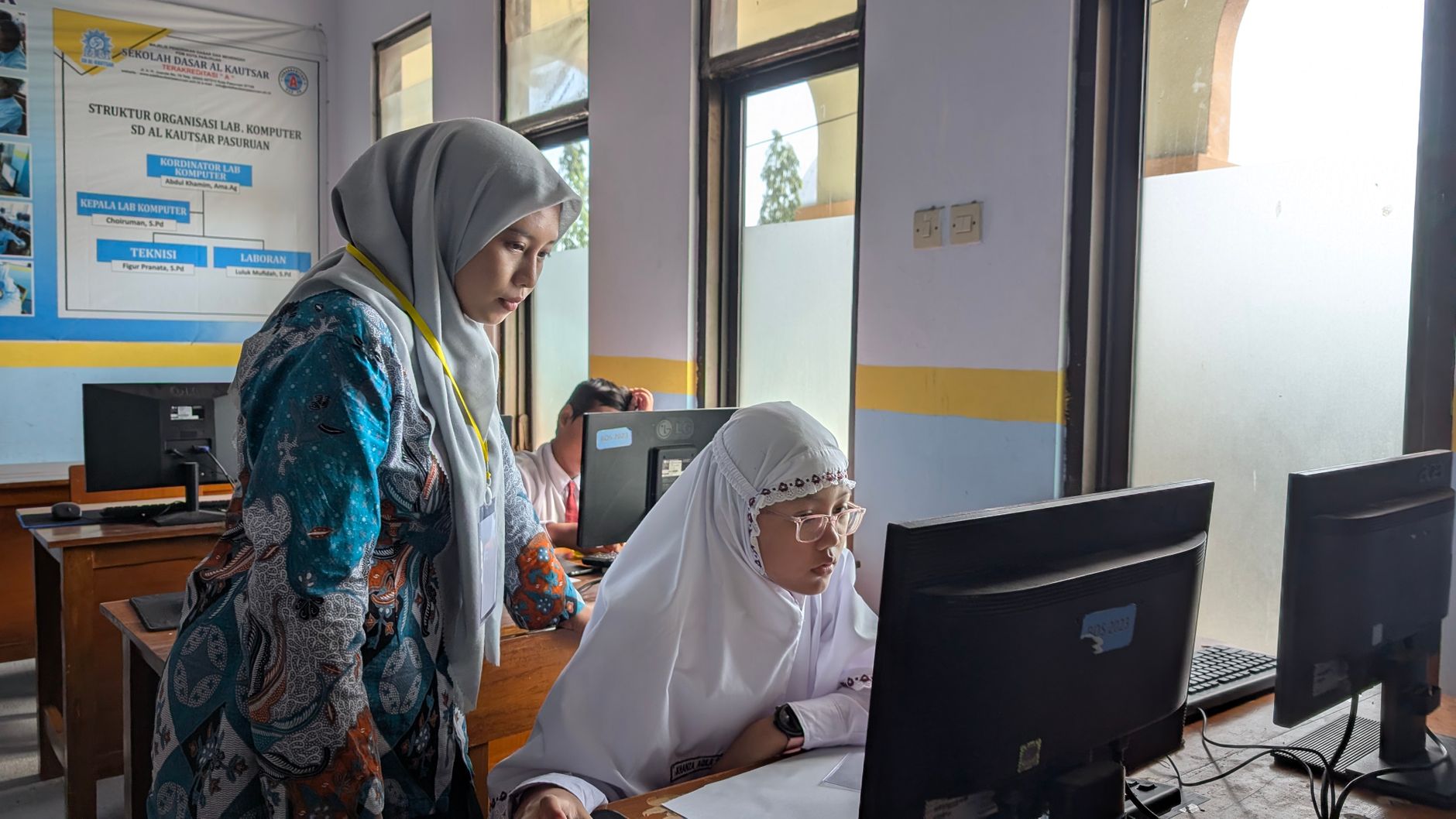 The Manager’s Toolkit — A female teacher guides a student working on a computer in a school lab, fostering learning.
