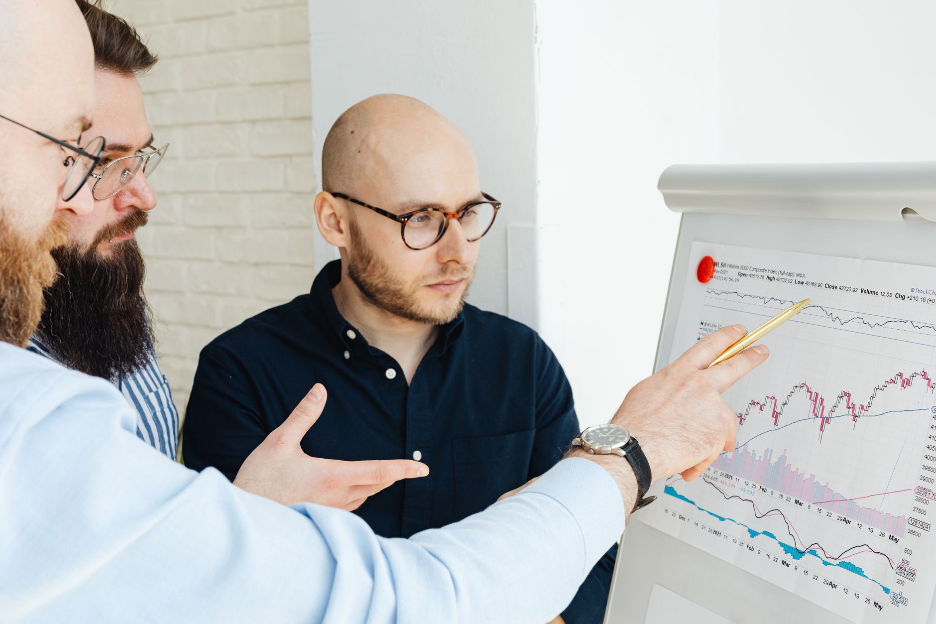 Innovation and Growth in Organisations — Three men discussing financial charts on a whiteboard during a business meeting.