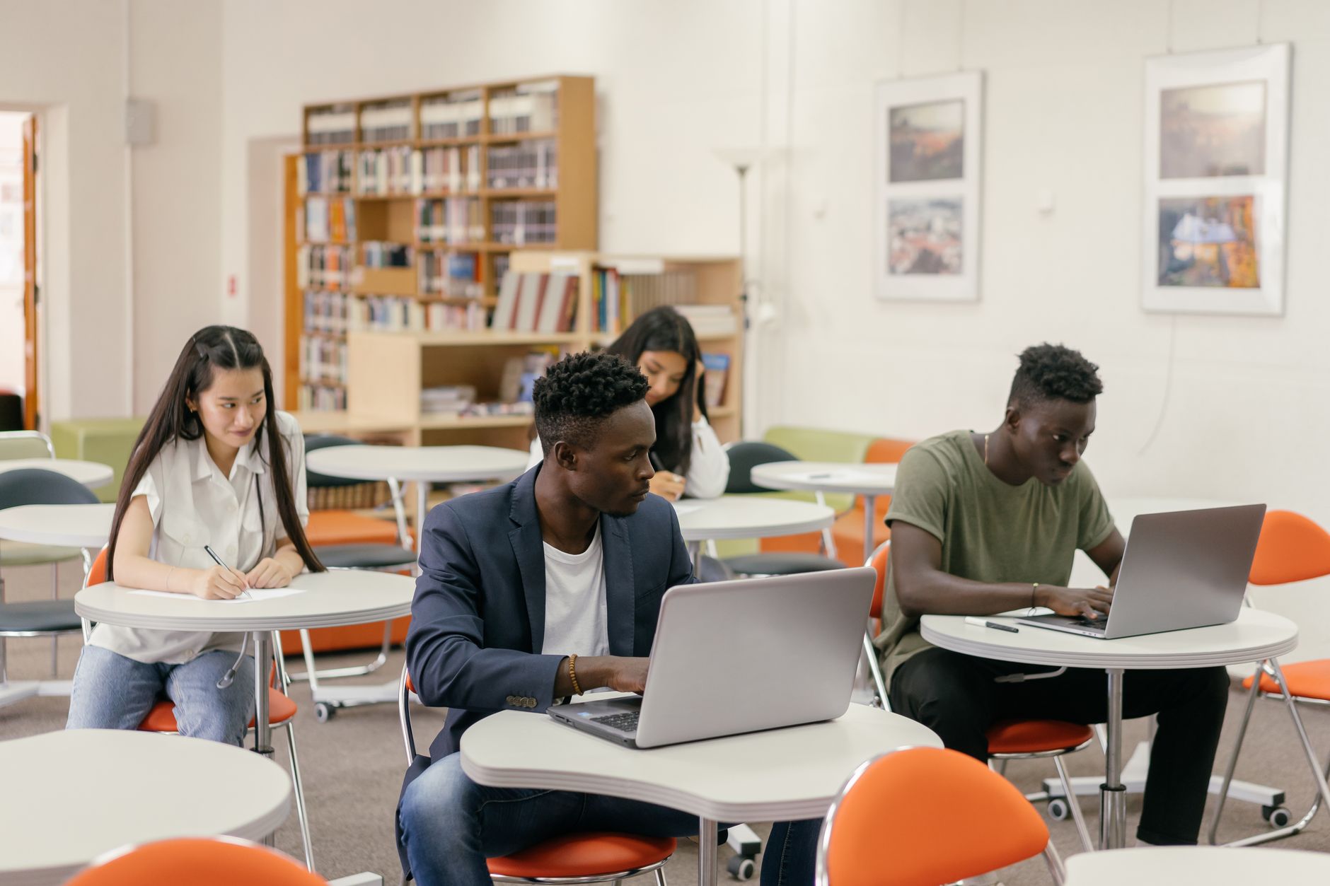 Principles of Research and Testing Innovative Ideas — Students focused on laptops and notes in a bright classroom setting.