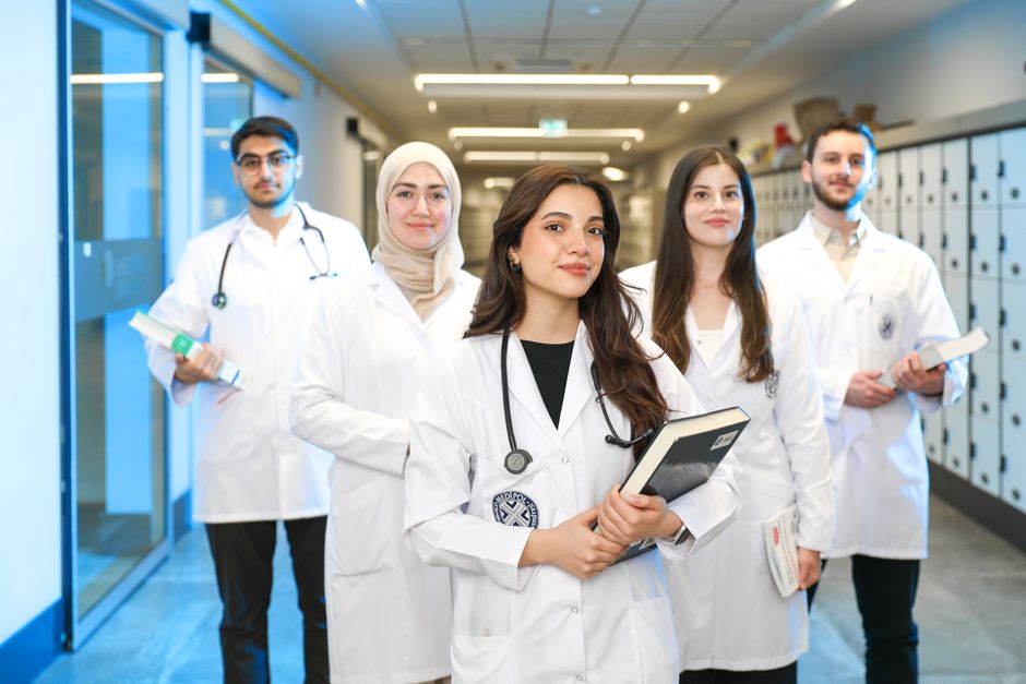 Qualifi Level 7 Diploma in Integrative Sport and Exercise Nutrition — Group of diverse medical students wearing lab coats in university corridor, representing future healthcare professionals.