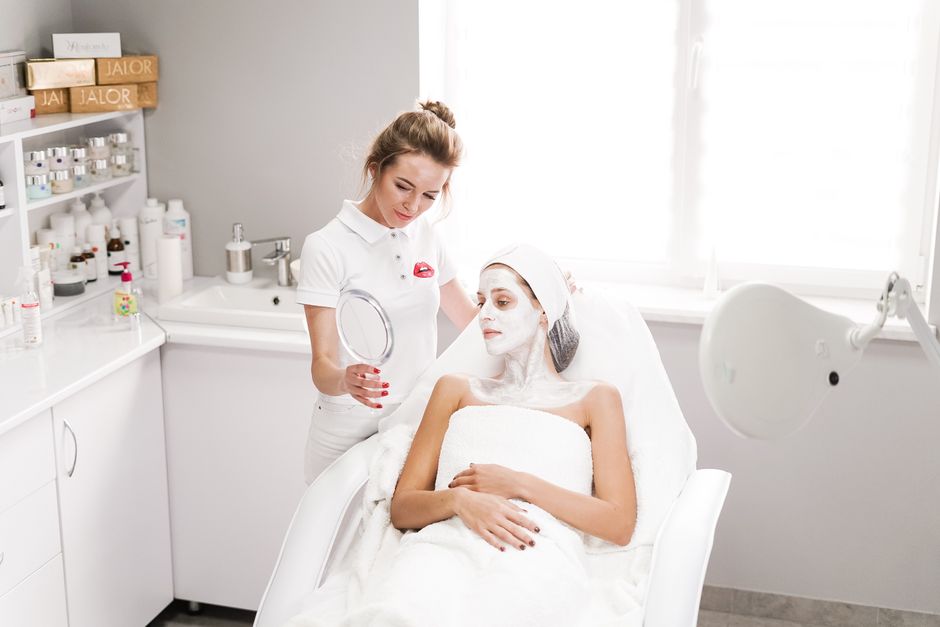 Qualifi Level 4 Certificate in Micropigmentation to Enhance Eyebrows — Beautician applying a facial mask to a client in a modern salon. Professional skincare service indoors.
