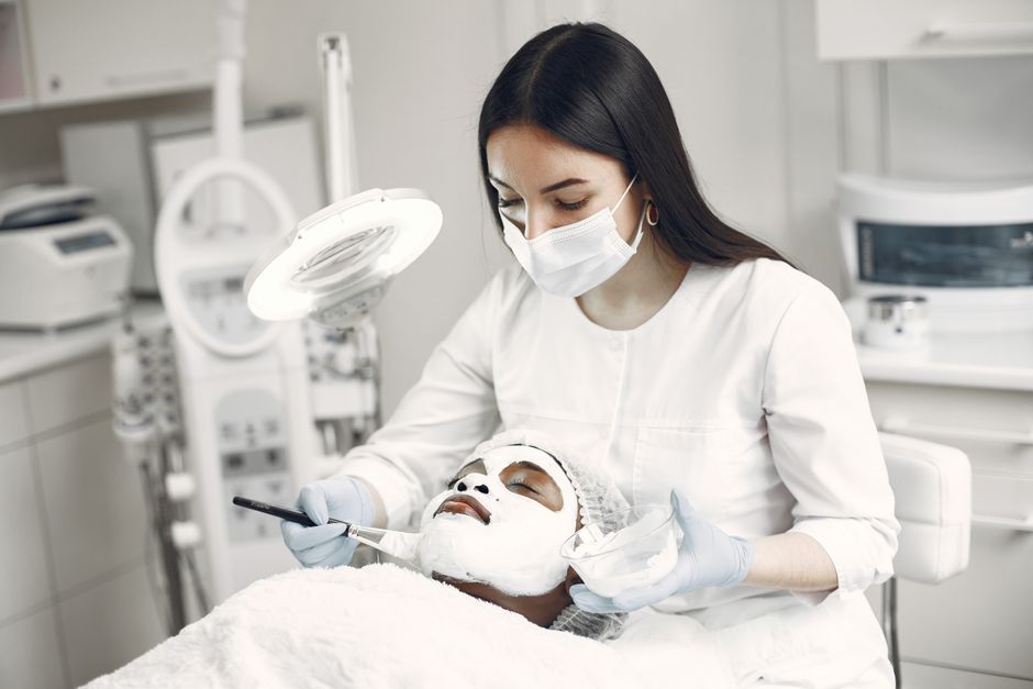 Qualifi Level 5 Certificate in Advanced Aesthetic Procedures: Micro-needling — A spa professional applying a facial mask to a client in a modern clinic setting.