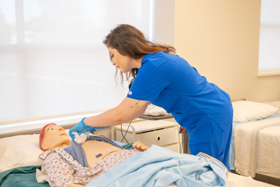Qualifi Level 3 Certificate in Anatomy, Physiology and Pathology — A nurse in blue scrubs trains on a medical dummy in a healthcare facility.