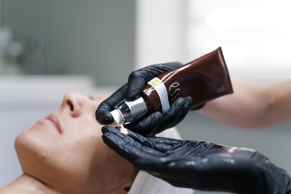 Qualifi Level 3 Diploma in Massage Therapy — Close-up of a skincare professional applying cream with gloves during a facial treatment in a clinic.