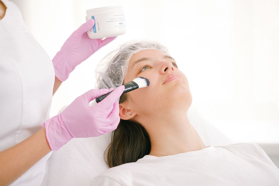Qualifi Level 3 Certificate in Thai Massage — A woman undergoing a facial treatment in a clinic by a professional using a brush and ointment.
