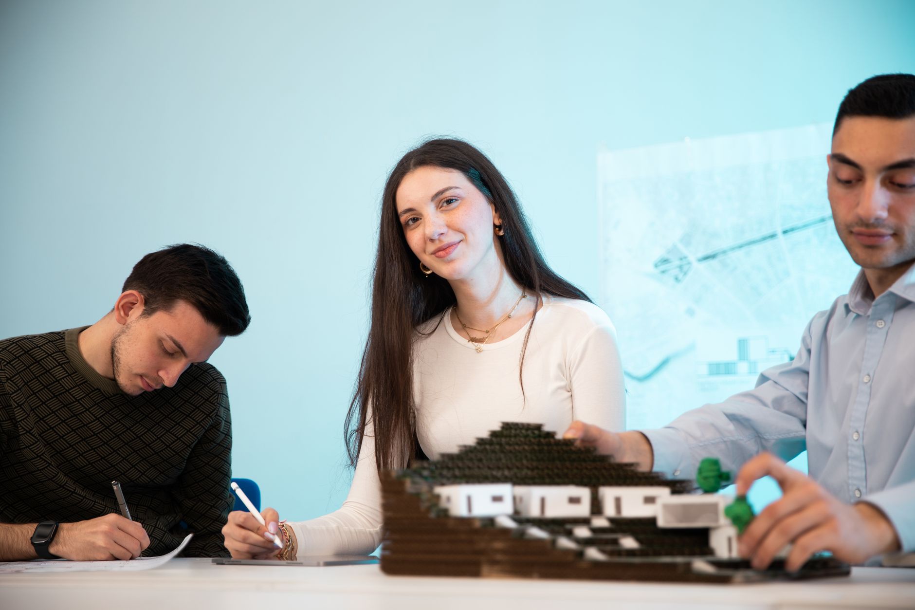 Business Models and Growing Organisations — Three people collaborating on an architectural model in an office setting, emphasizing teamwork.