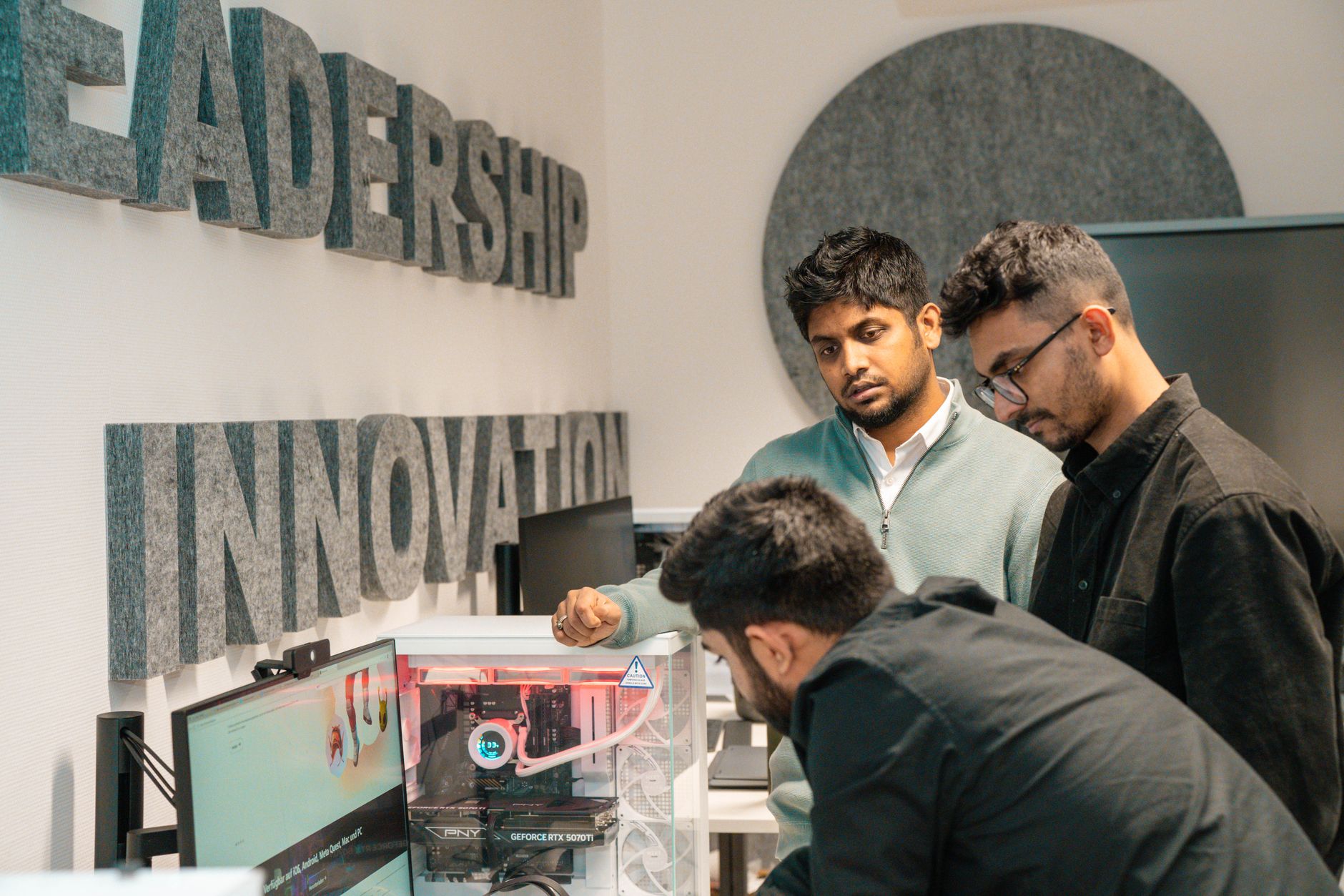 Creative and Innovative Management — Three men collaborate in an office, focusing on tech innovation. leadership and team dynamics emphasized.