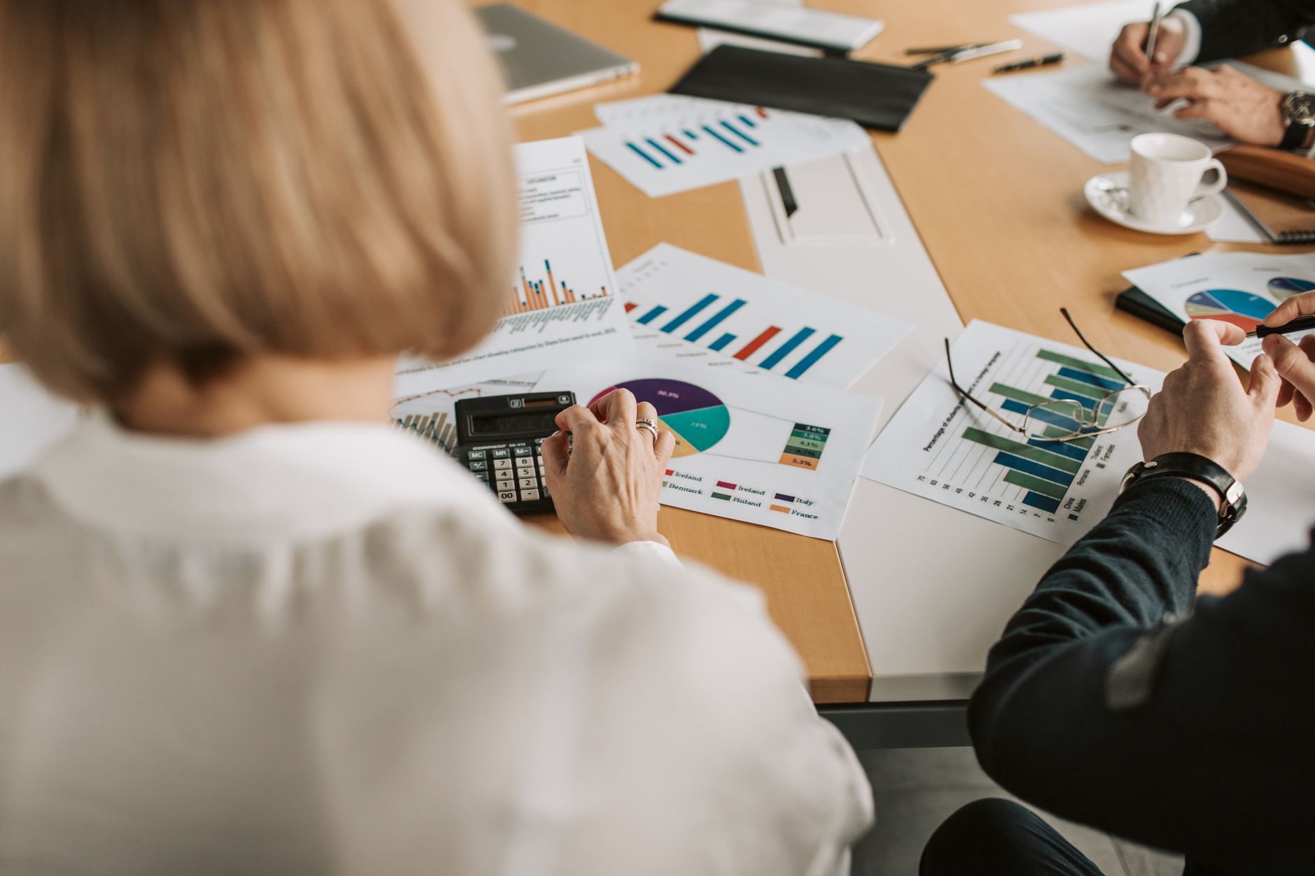 Business Finance — Overhead view of professionals discussing financial graphs and using calculators in an office setting.