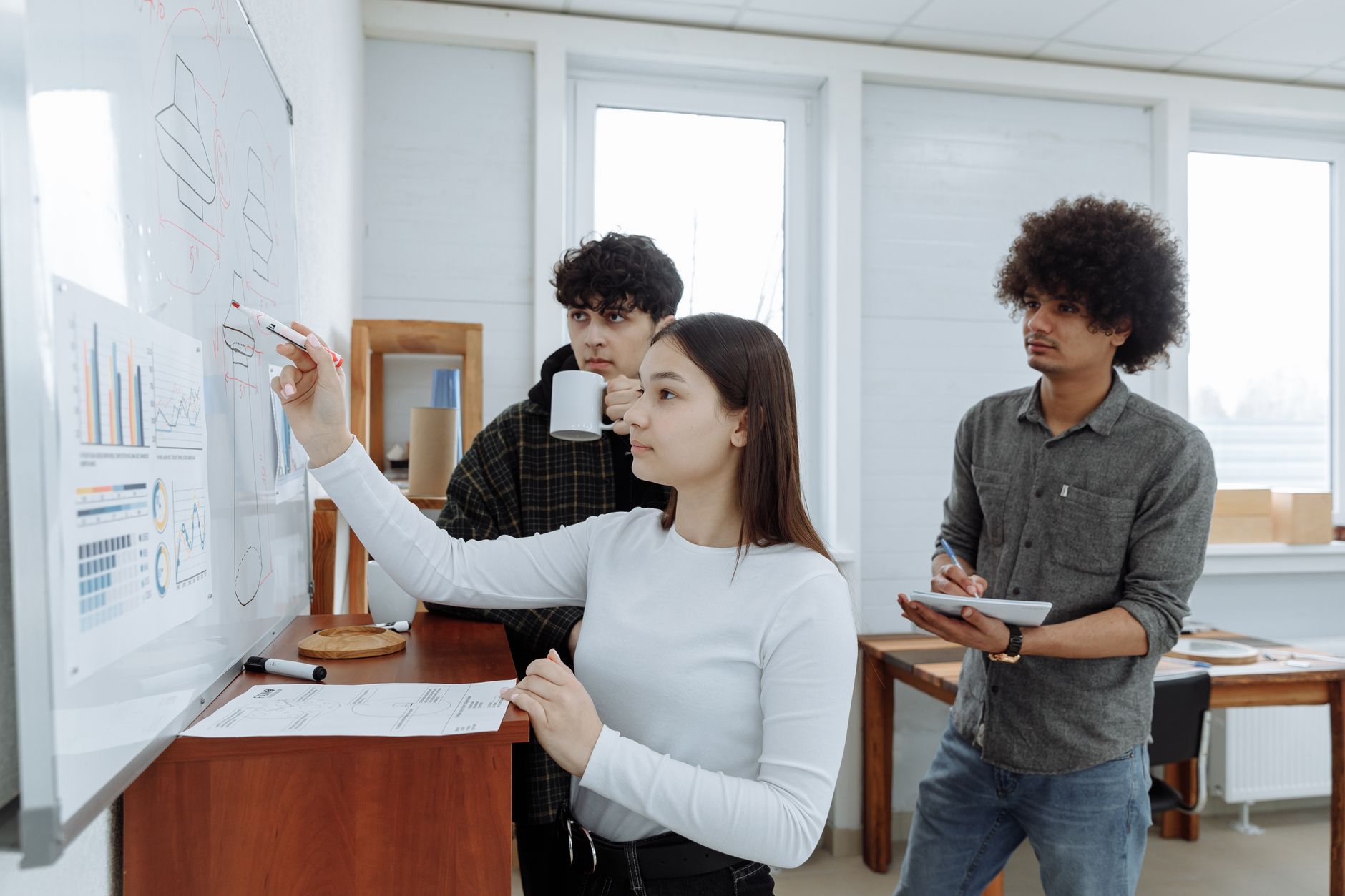 Planning, Controlling and Leading a Project — Three team members plan and collaborate at a whiteboard in a modern office setting.