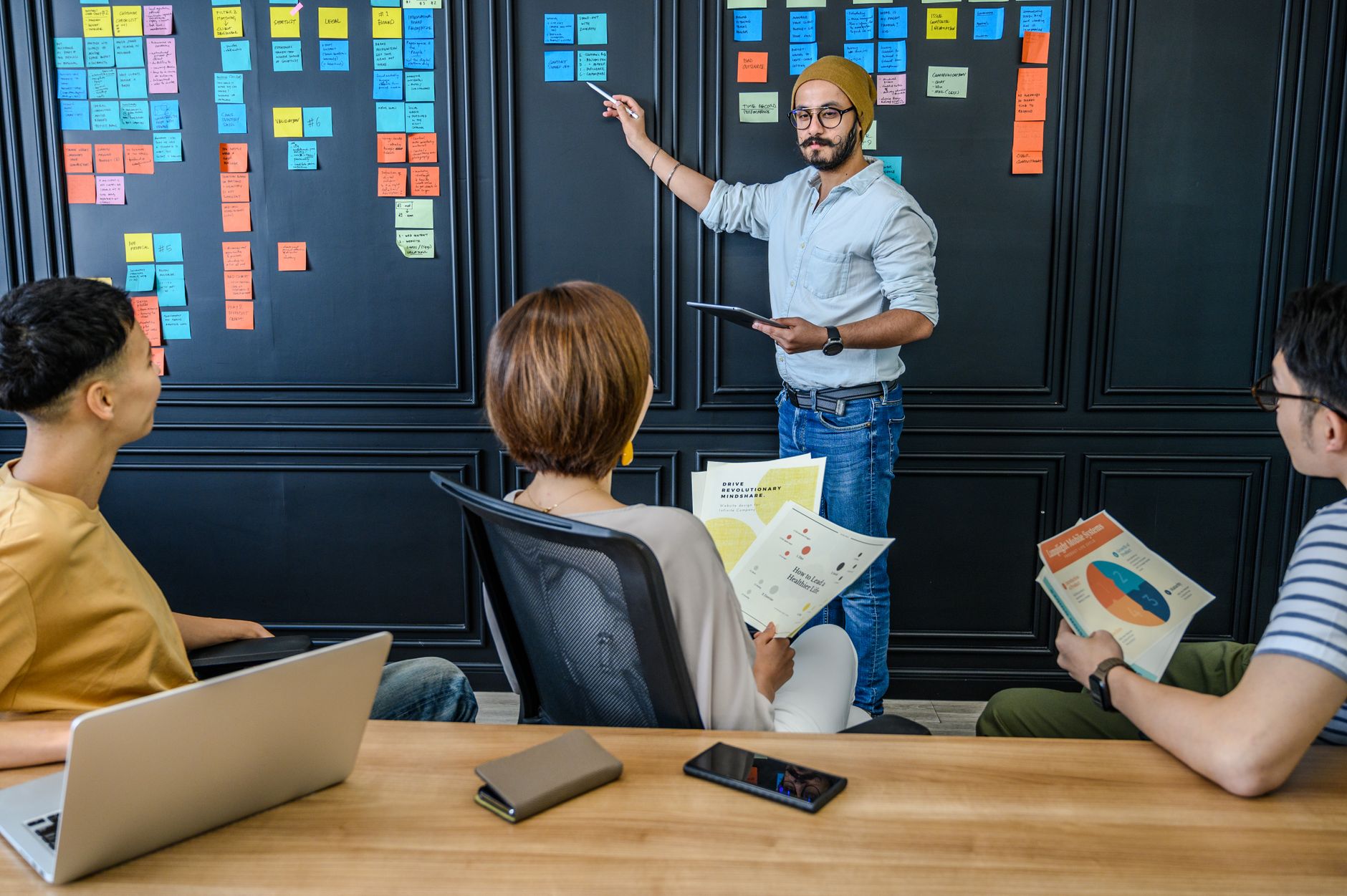 Project Management — Diverse team collaborating in a modern office environment with sticky notes and charts.