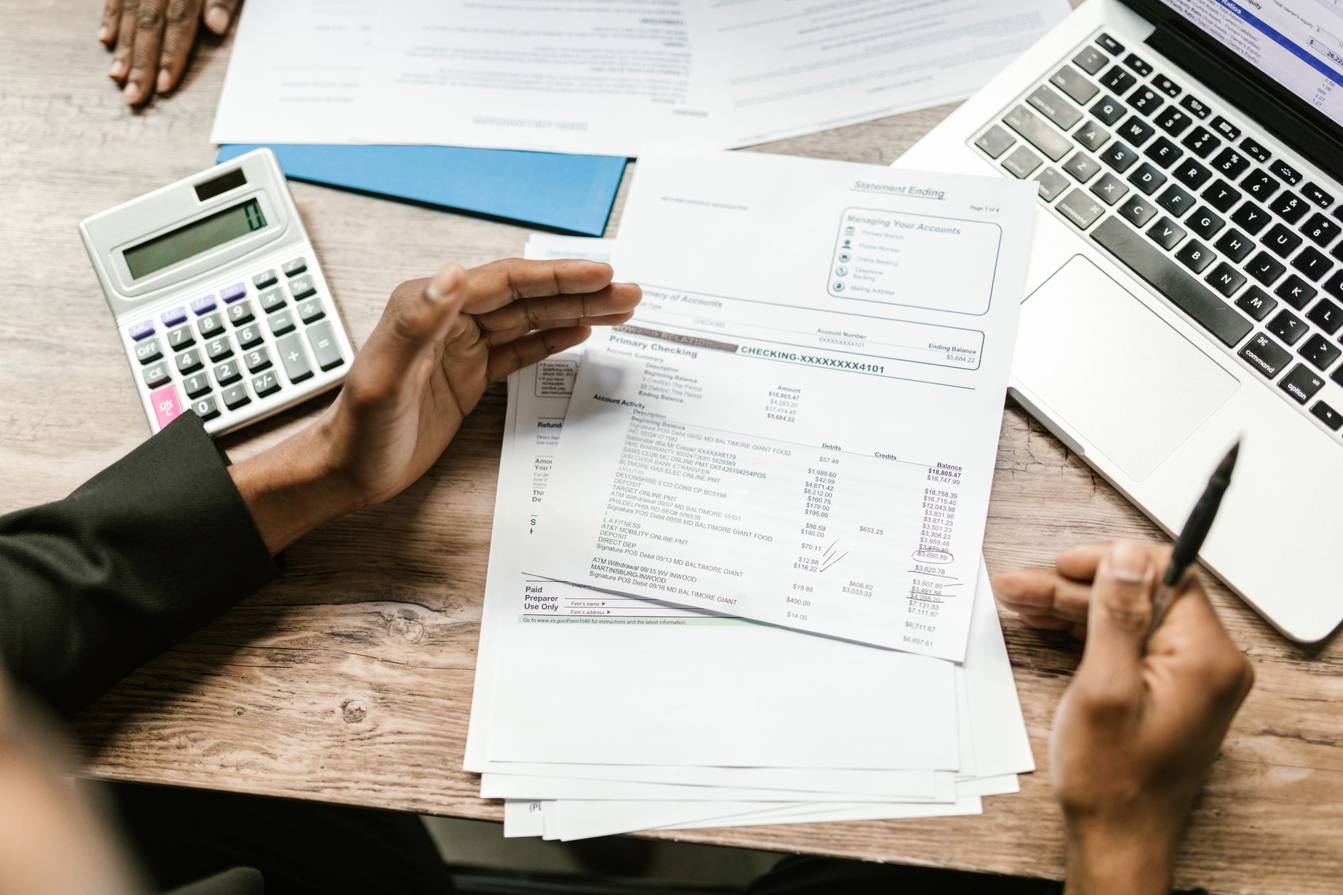 Finance for Managers — Hands holding financial documents with calculator and laptop on office desk, business analysis scene.