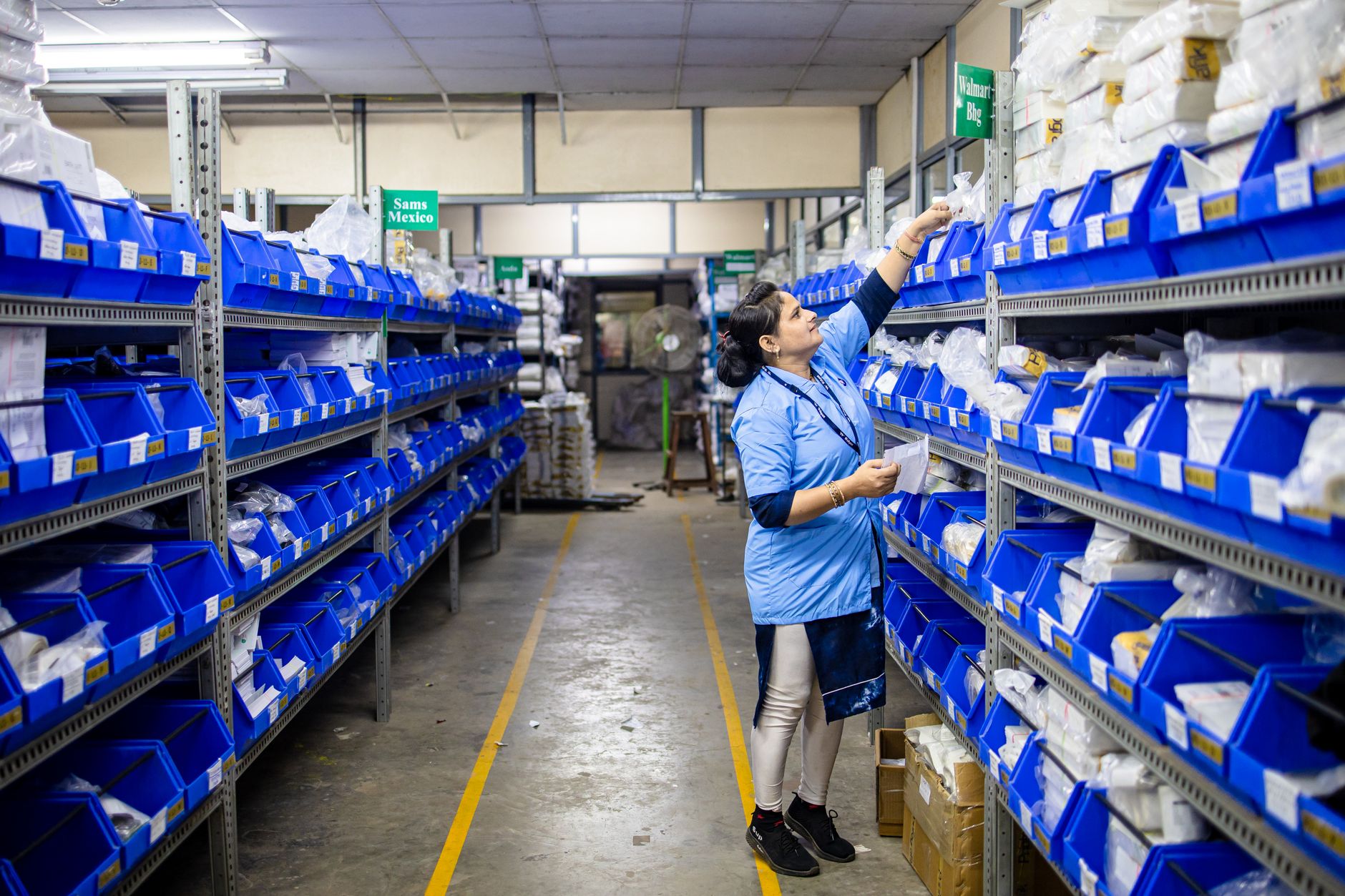 Project and Logistics Management — Woman in uniform organizing inventory in a warehouse aisle with labeled bins.