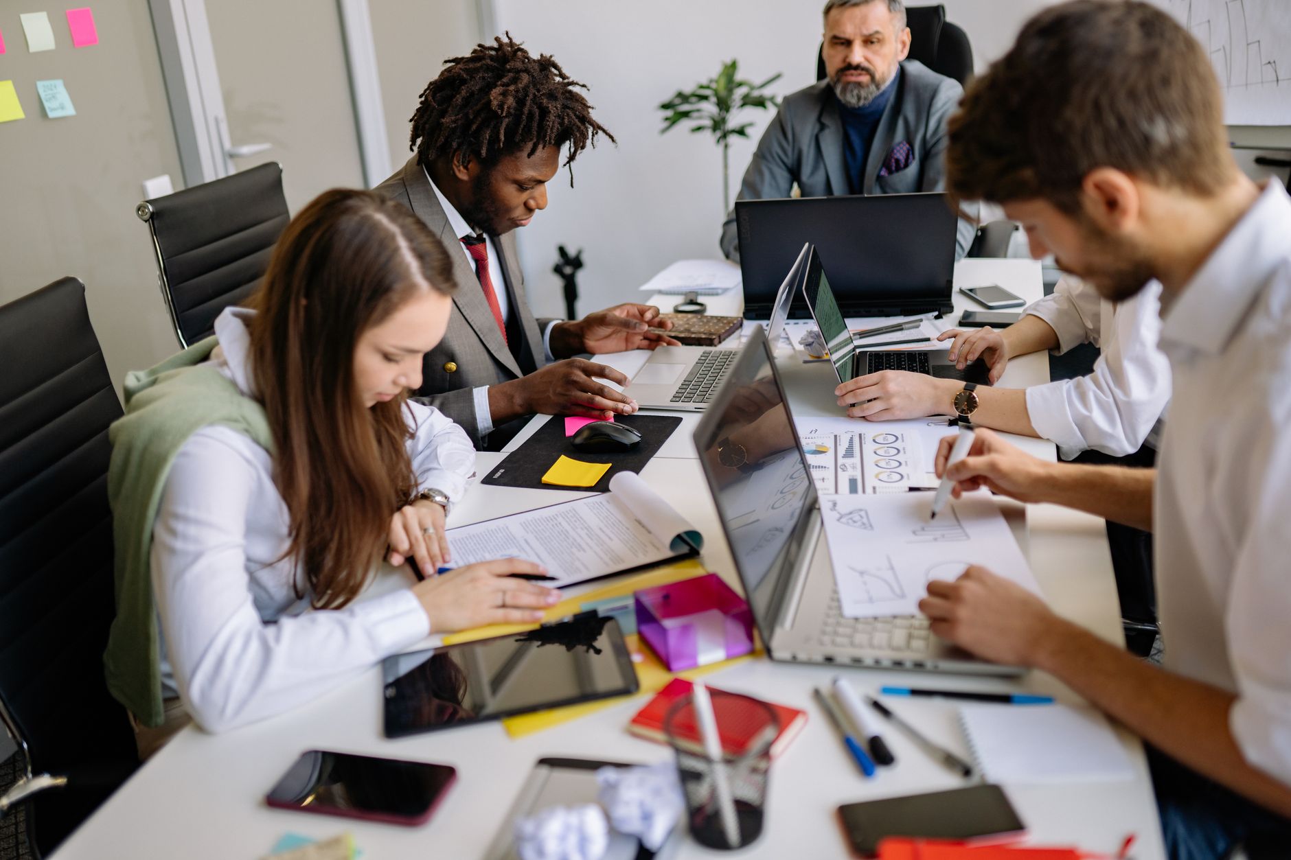 Strategy Development in Cross Border and Global Organisations — Team of professionals collaborating around a table in a modern office, focusing on projects and discussions.