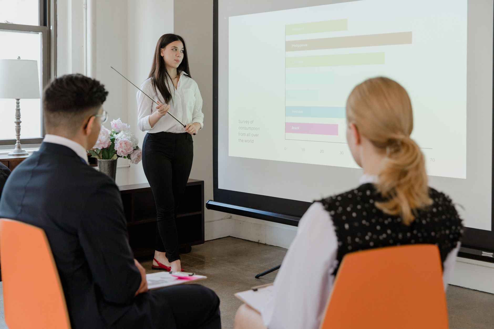 Strategic Communication — A young professional presenting data in a modern office to attentive colleagues.