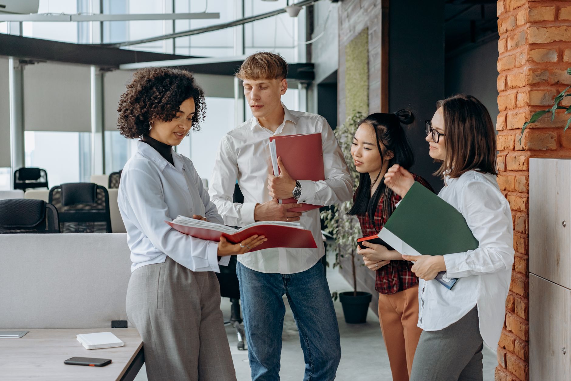 Research Methods — Four colleagues collaborating on documents in a modern office setting, emphasizing teamwork and diversity.