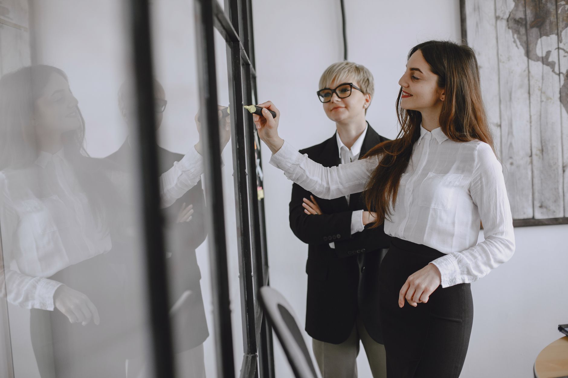 Strategic Brand Management — Two professional women collaborating in a modern office setting, focusing on teamwork and strategy.