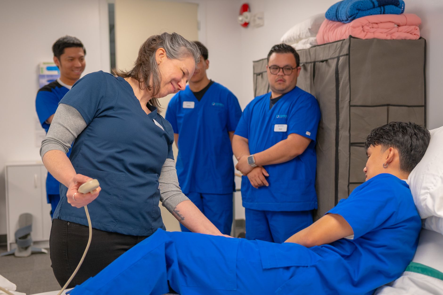 Assist in the Administration of Medication — Healthcare professionals in a training session using medical equipment indoors.