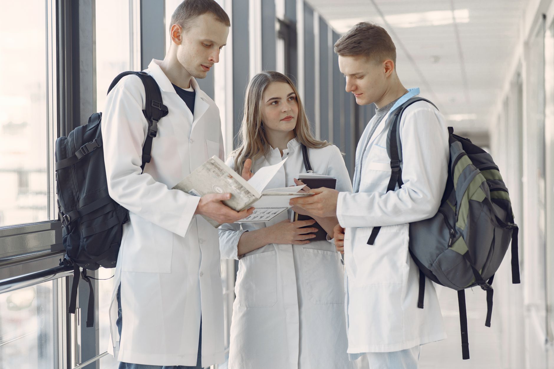 Enable Individuals to Develop Strategies to Manage Behaviour — Three medical students in a hospital hallway sharing notes and learning together.