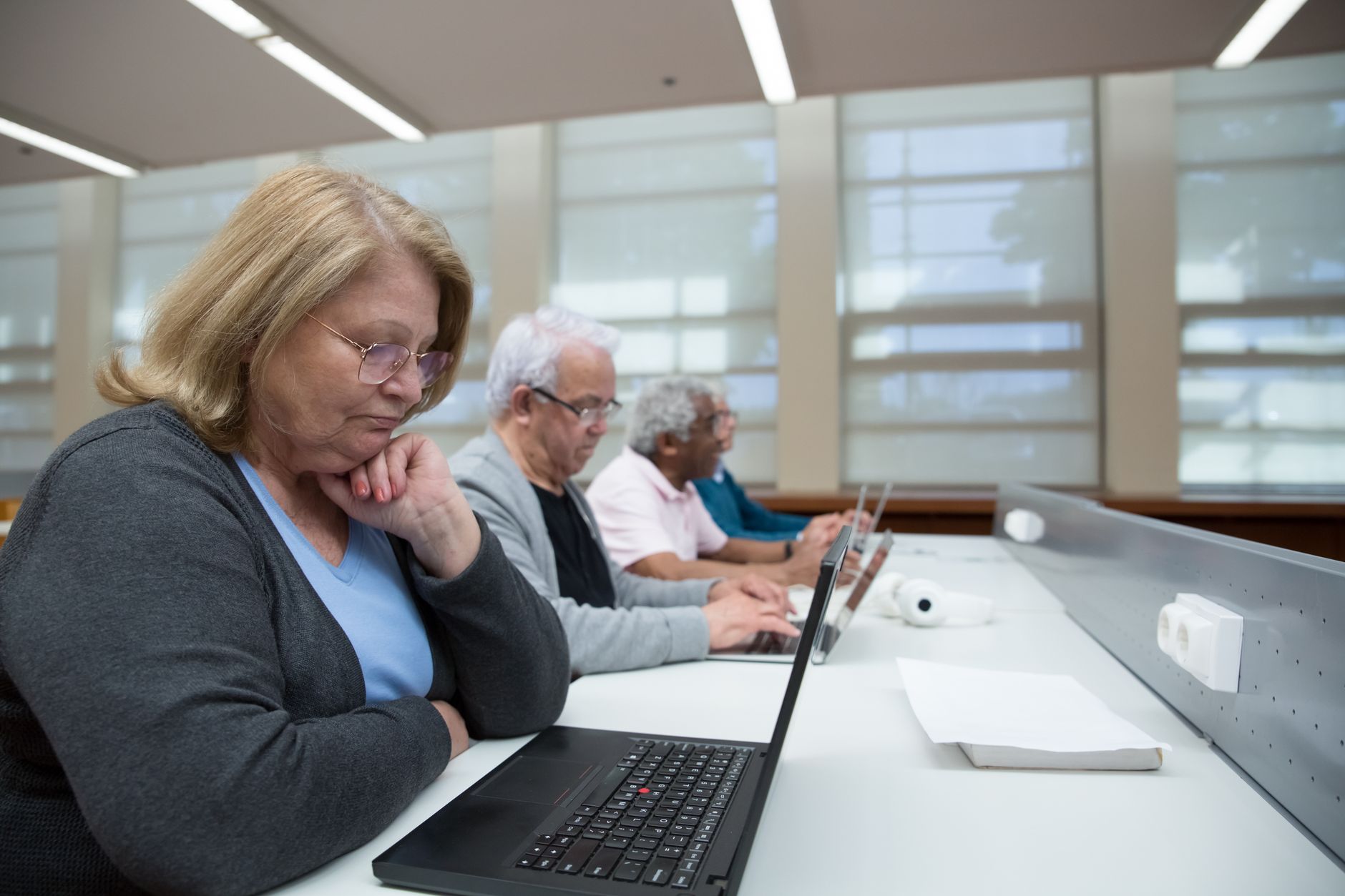 Privacy and Dignity — Seniors engaged in a computer class, learning digital skills with laptops indoors.