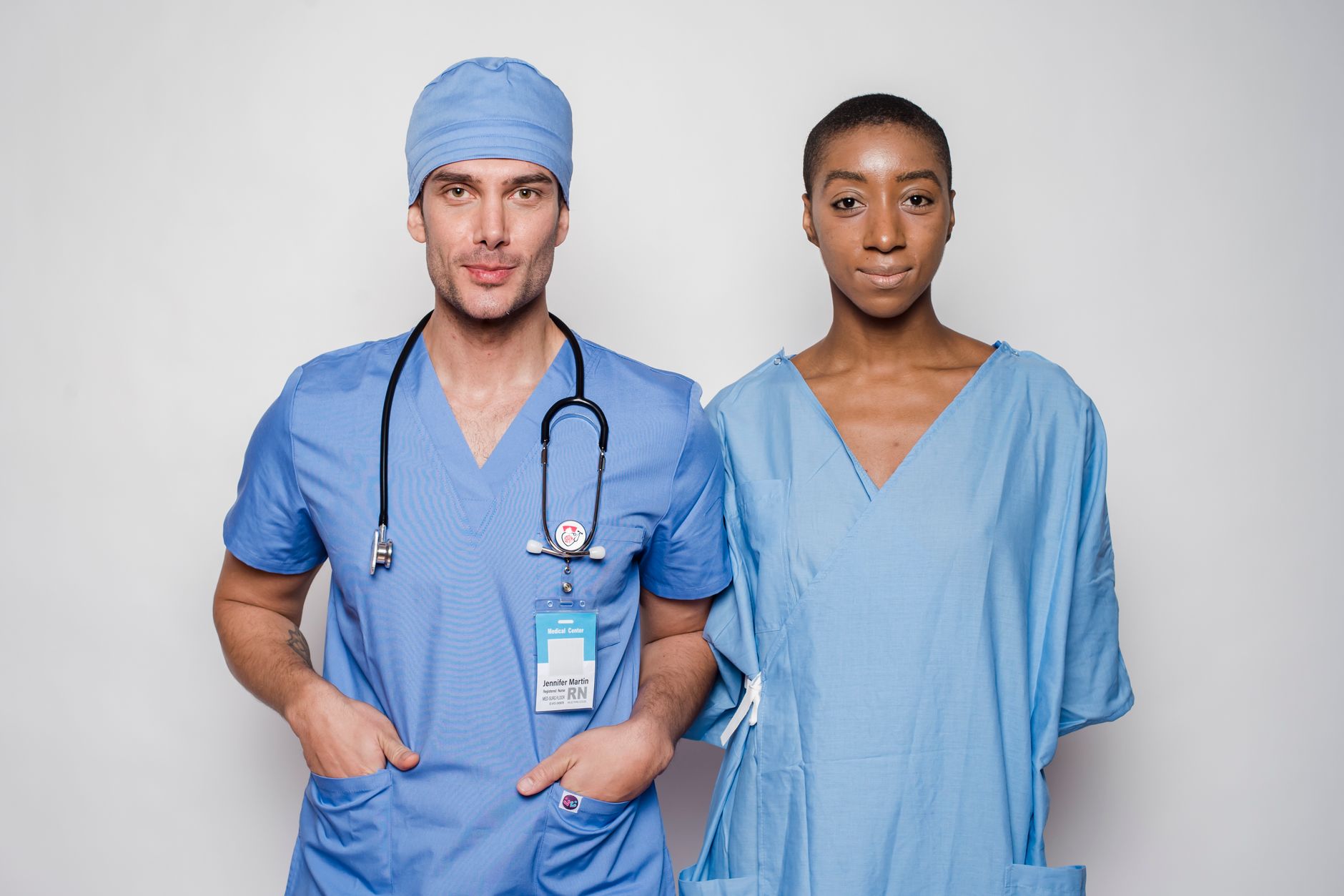 Promoting Health in the Population — Positive male doctor in blue uniform with hands in pockets smiling and looking at camera while standing near nurse holding hands behind back in hospital