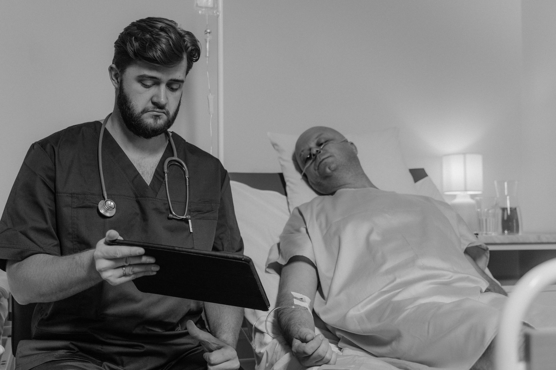 Sociology Concepts in Health and Ill Health — A doctor reviews a patient's medical records on a digital tablet in a hospital room.