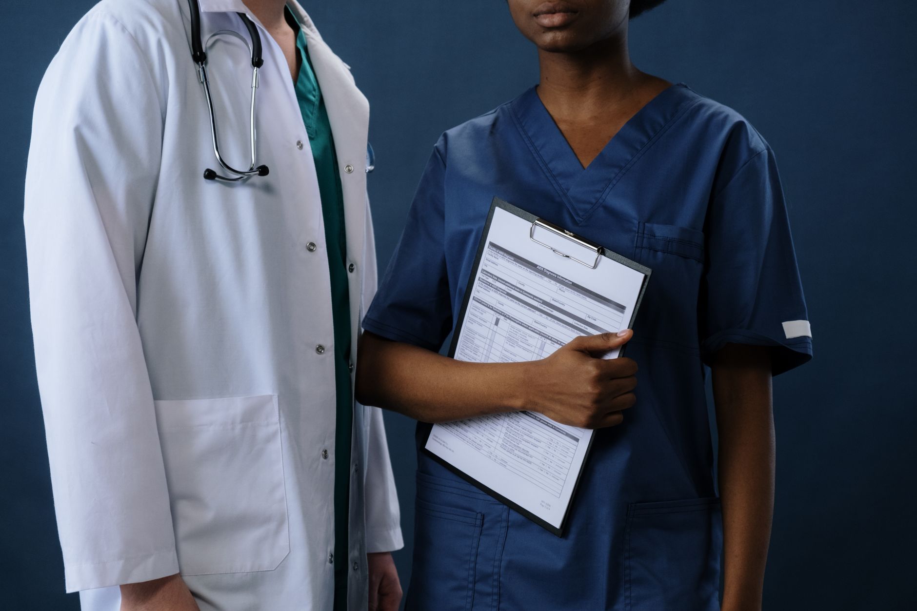 Managing Finance in Health and Social Care — Two healthcare professionals in scrubs and lab coat with a clipboard, representing teamwork.