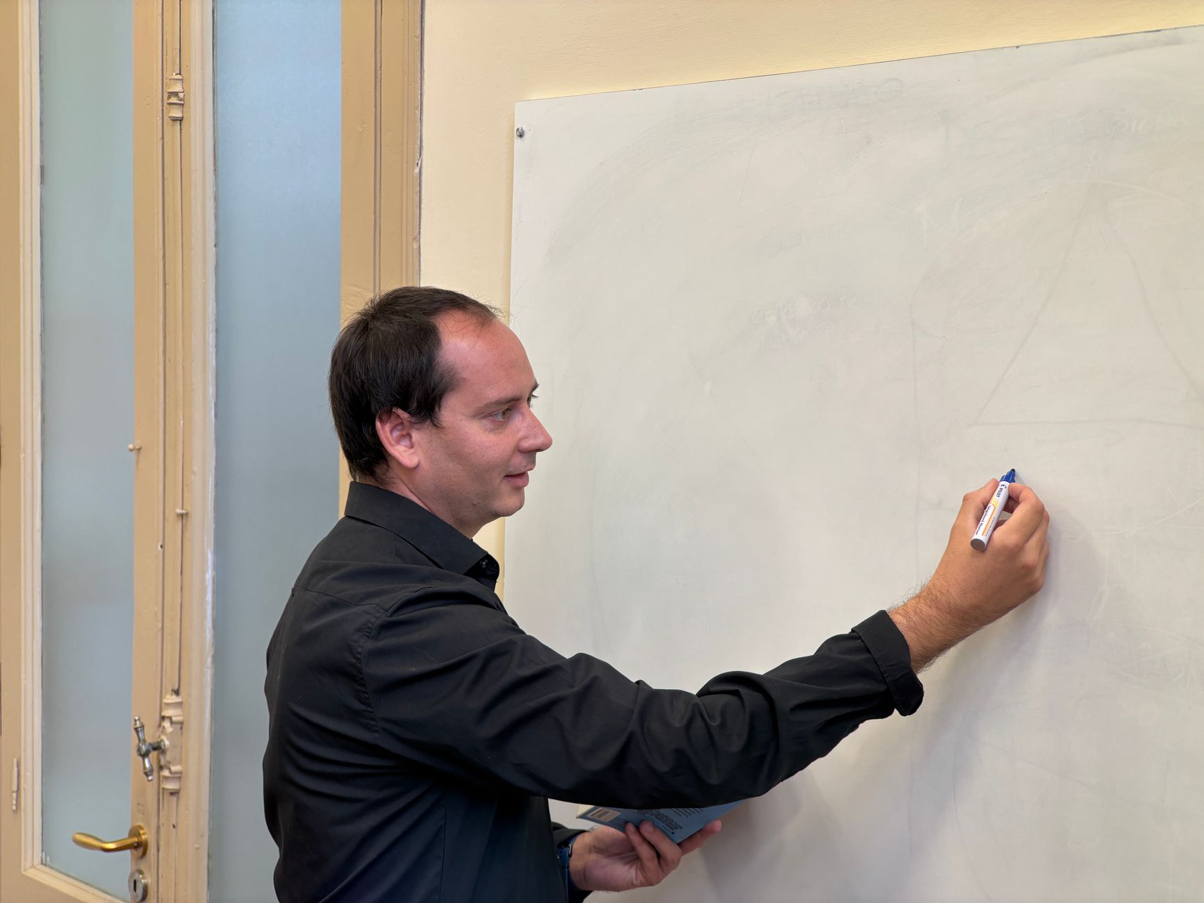 Contemporary Issues and Debates in Psychology — A male teacher writing on a whiteboard in a classroom setting.