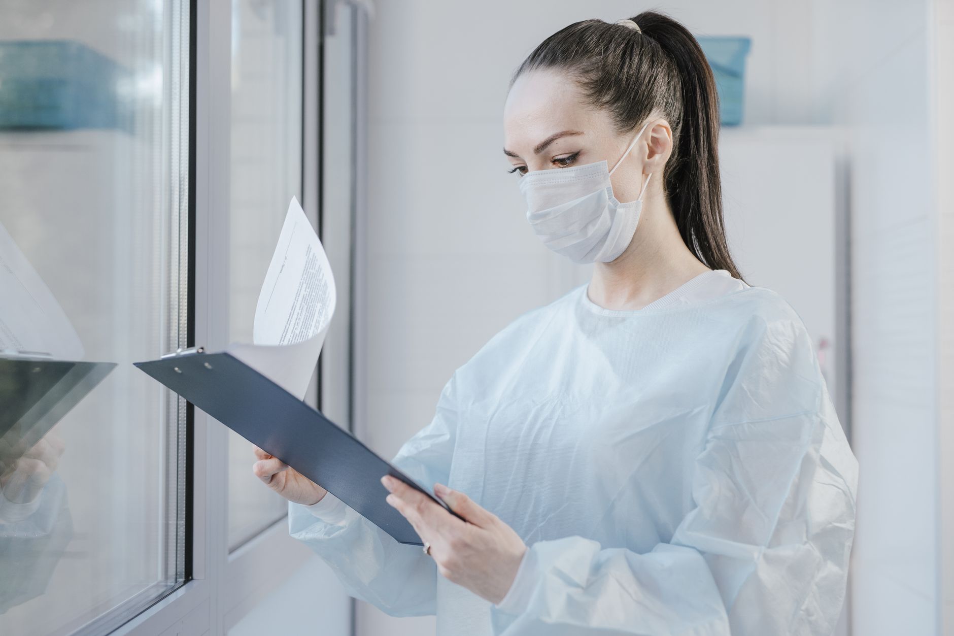 Health and Safety Management Practice — A female doctor in a mask examining patient's medical records in a hospital setting.