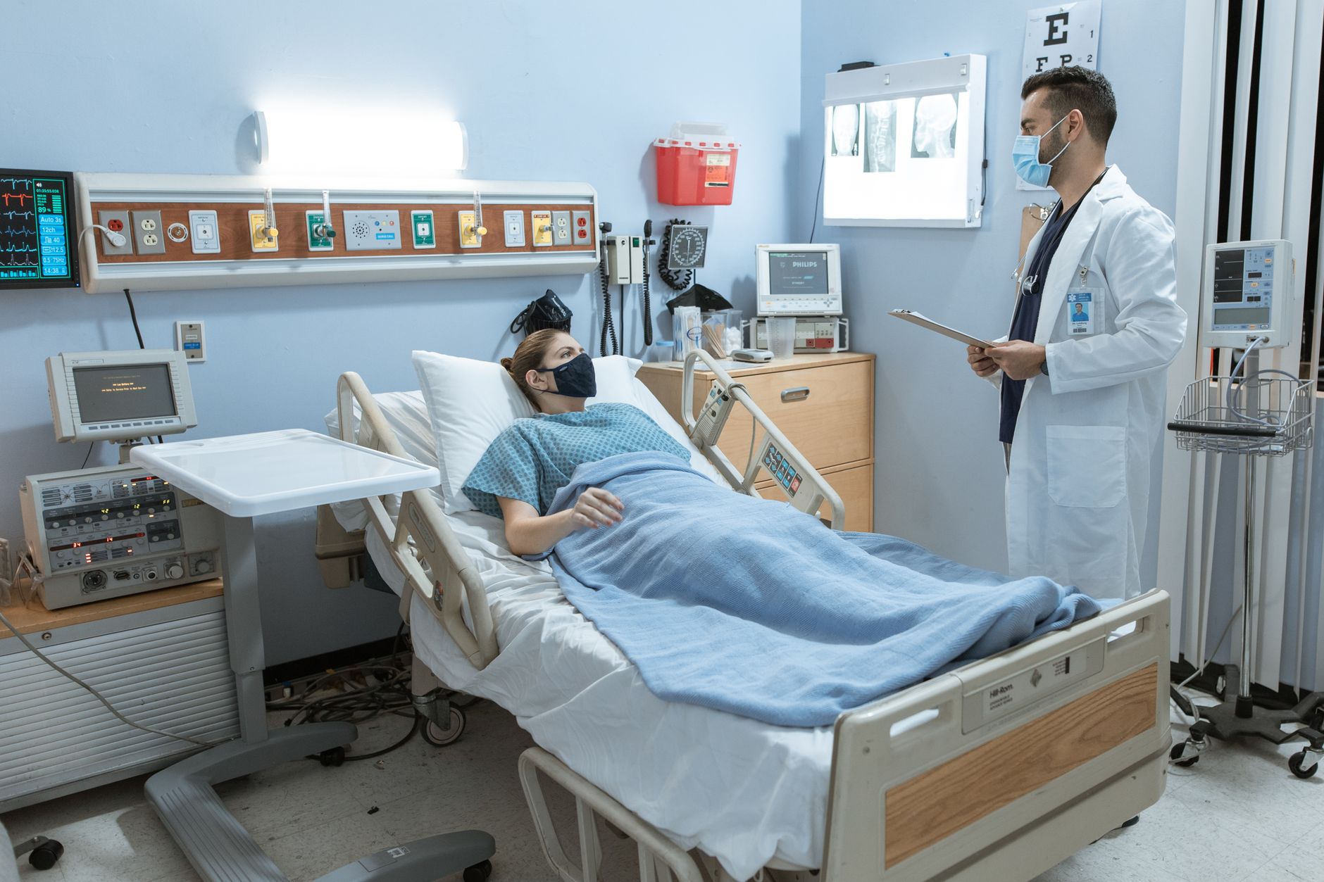 Factors Affecting Risk and Strategic Risk Intervention — A doctor checking on a patient in a hospital room, both wearing face masks for safety.
