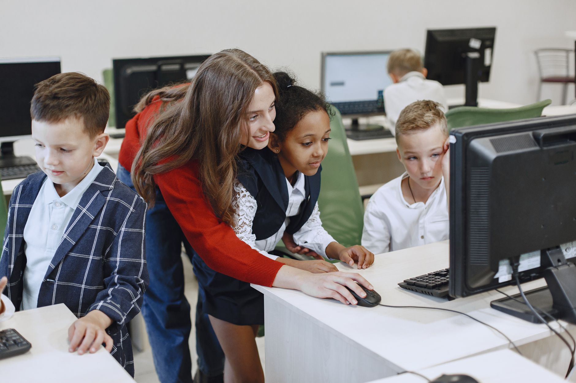 Management of Visitor Attractions — Teacher engaging with diverse children in a technology lesson using computers in a modern classroom.