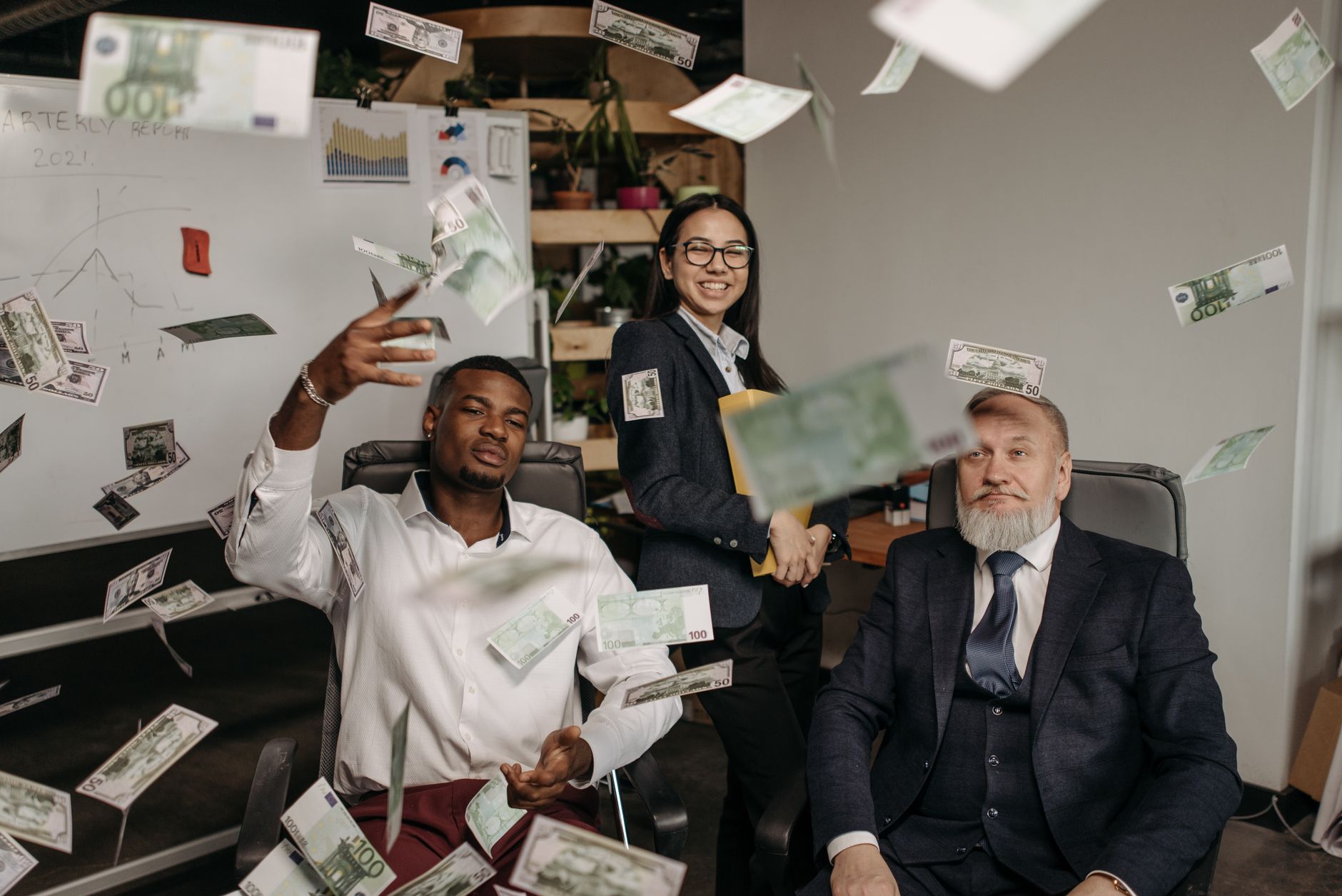 Financial Management — Diverse business team celebrating success with cash raining indoors in office.