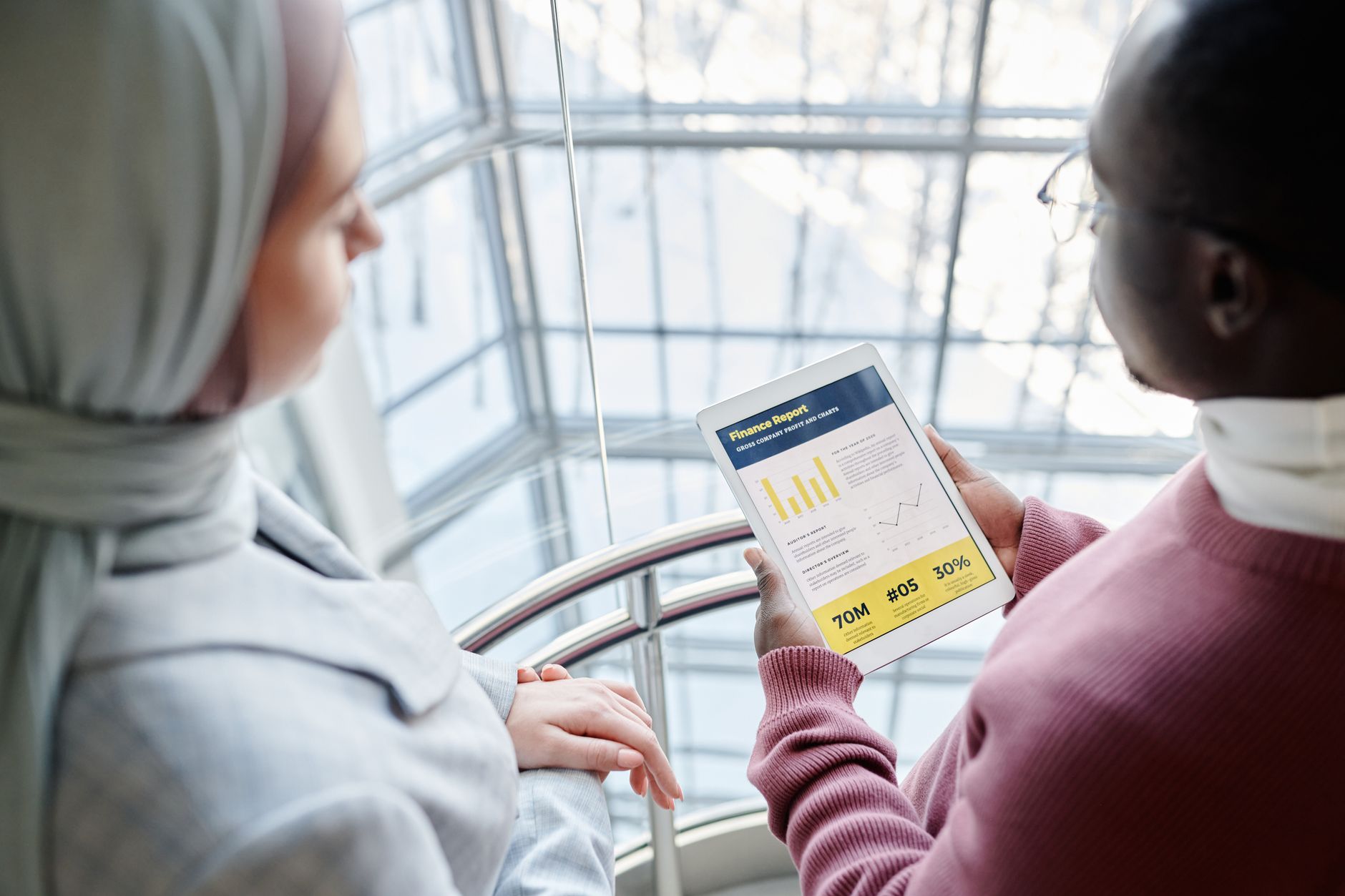 Corporate Reporting — Two business professionals discussing financial data on a tablet in a modern office setting.