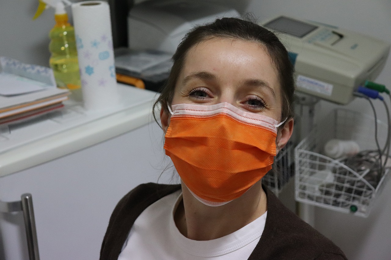 Understanding Health and Safety in the Business Workplace — Face mask, nurse, woman with mask, healthcare worker, orange mask, clinic, medical setting, safety, hospital, pandemic, protective gear, health professional, smiling eyes, female portrait, medical staff, friendly expression, covid-19, hygiene, healthcare environment, face protection, medical equipment, doctor, protective wear, indoor portrait
