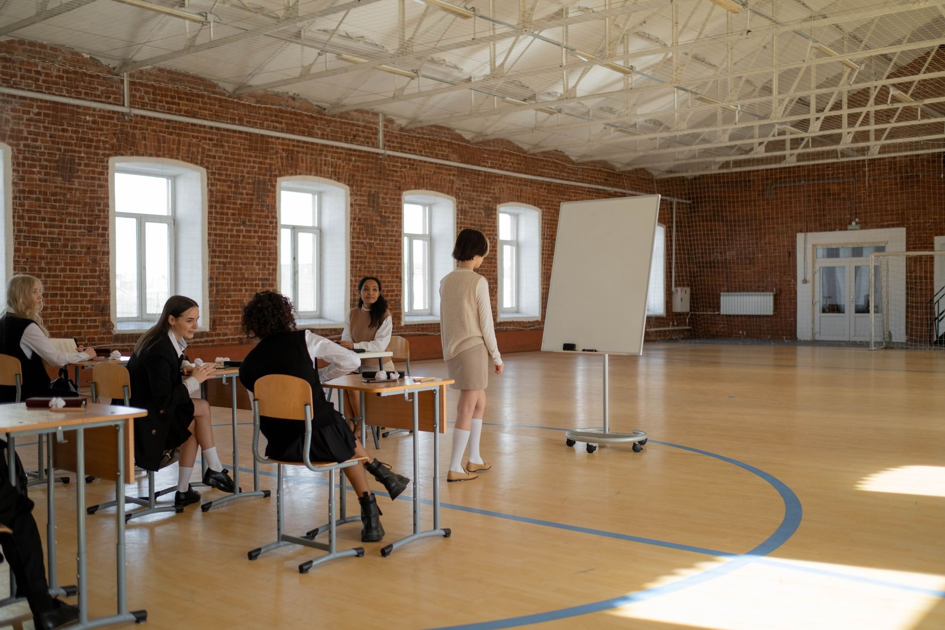 Managing Business Operations — Students in school uniforms engaged in a lesson with a teacher in a spacious classroom.