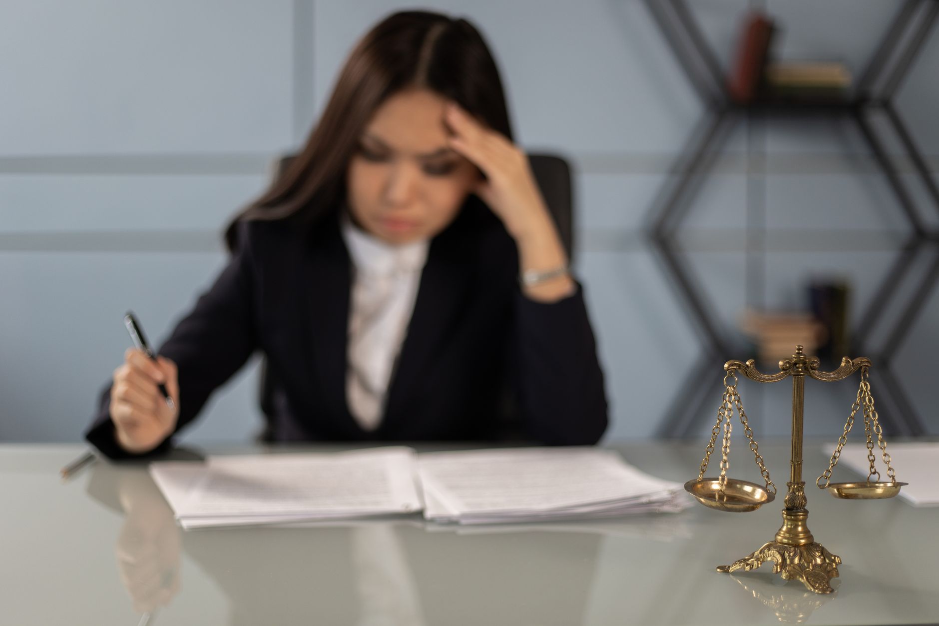 Corporate Governance – Principles and Practices — A fatigued female lawyer reviewing documents with a justice scale nearby, emphasizing stress in legal work.